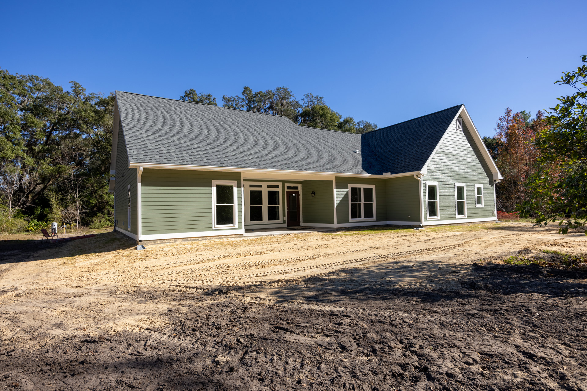 Two-story house with a large roof, multiple white-framed windows, dirt road and patch in front, surrounded by trees with Robert Frost Farm visible in the background