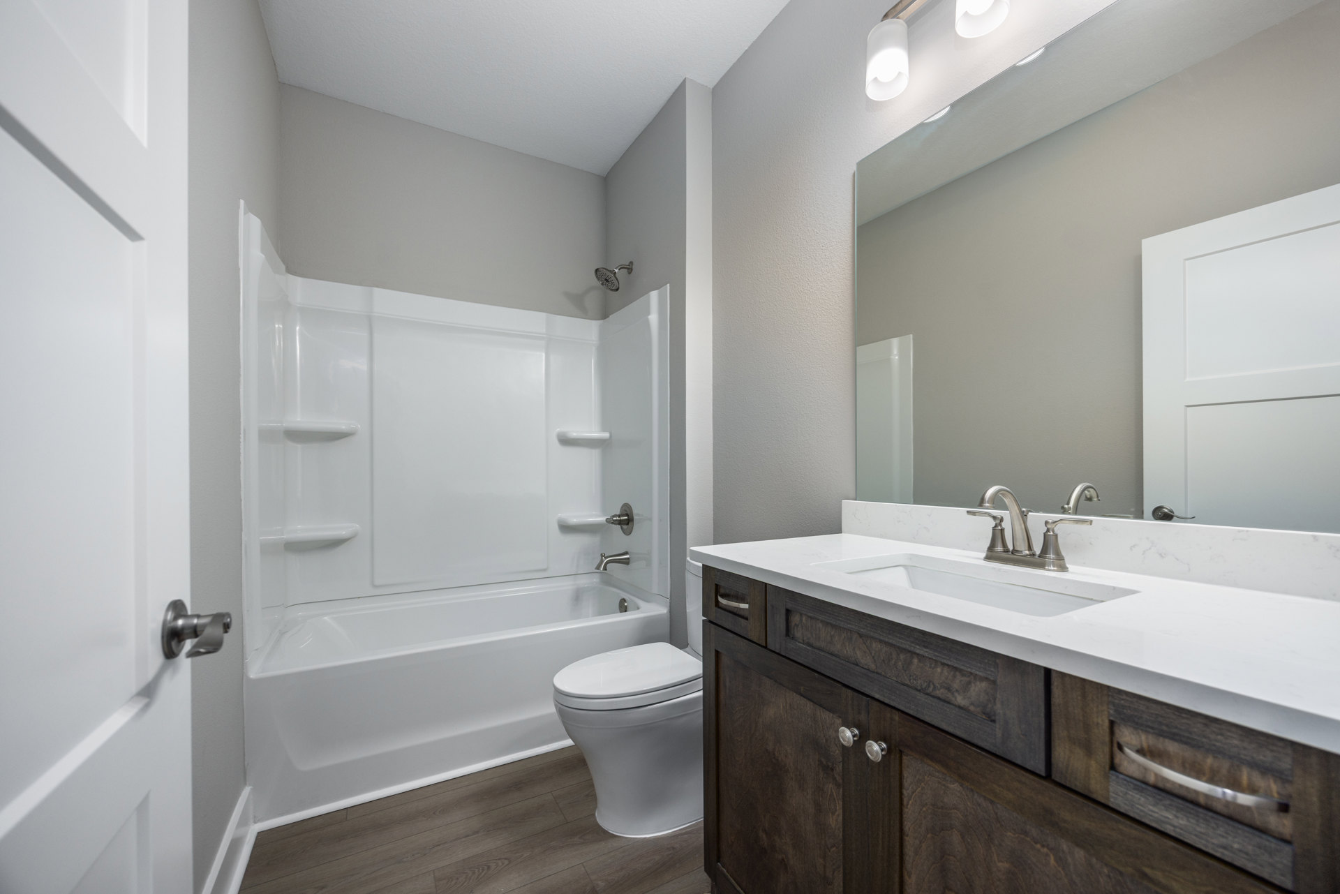 Bathroom with white toilet, white bathtub, sink with cabinets, tiled floor, and roll of toilet paper hanging on door handle