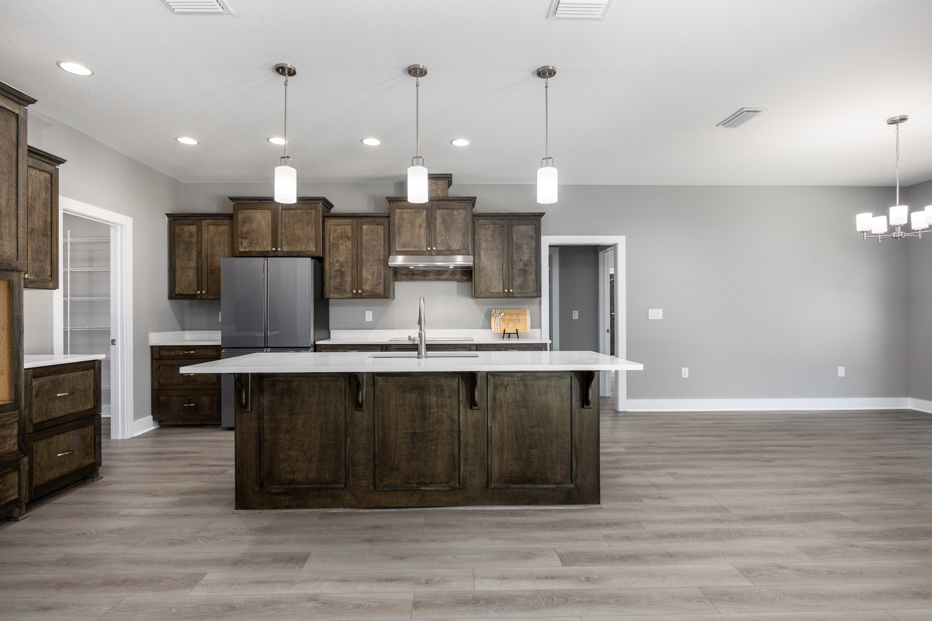Modern kitchen featuring a central island with a built-in sink and faucet, stainless steel refrigerator with glass doors, wood cabinetry, stone countertops, and pendant lighting