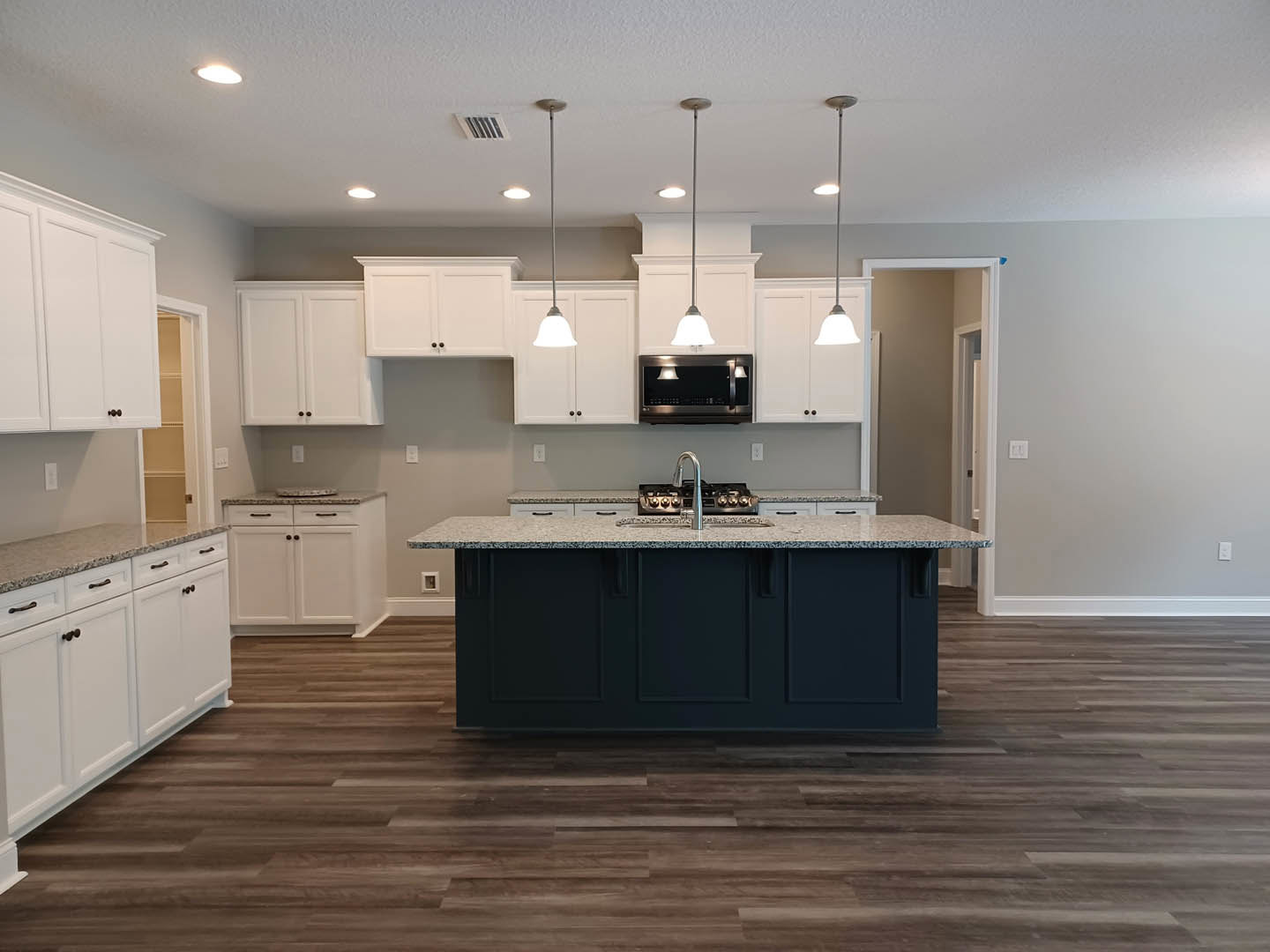 Kitchen with white shaker cabinets, central island with stone countertop, stainless steel sink and stove, dark wood flooring, recessed ceiling lights