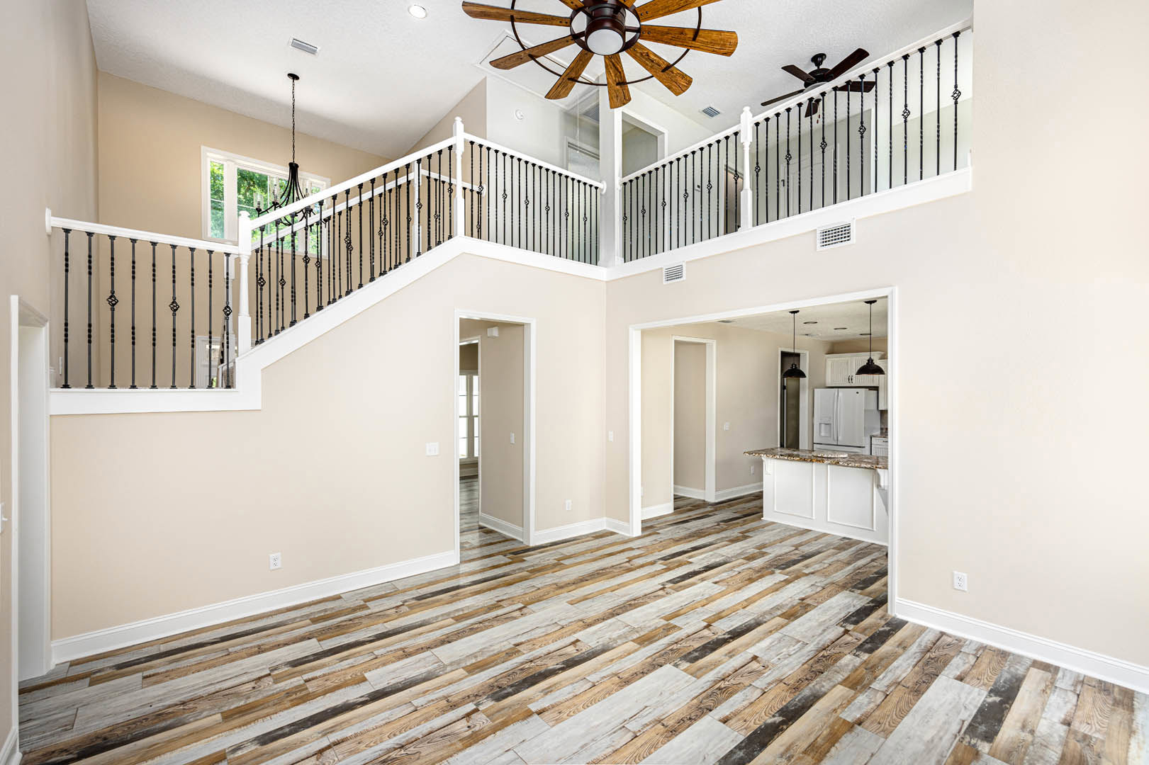 Open living area with wood flooring, white walls, ceiling fan with light, staircase featuring white balusters and wood handrail, adjacent kitchen with white refrigerator