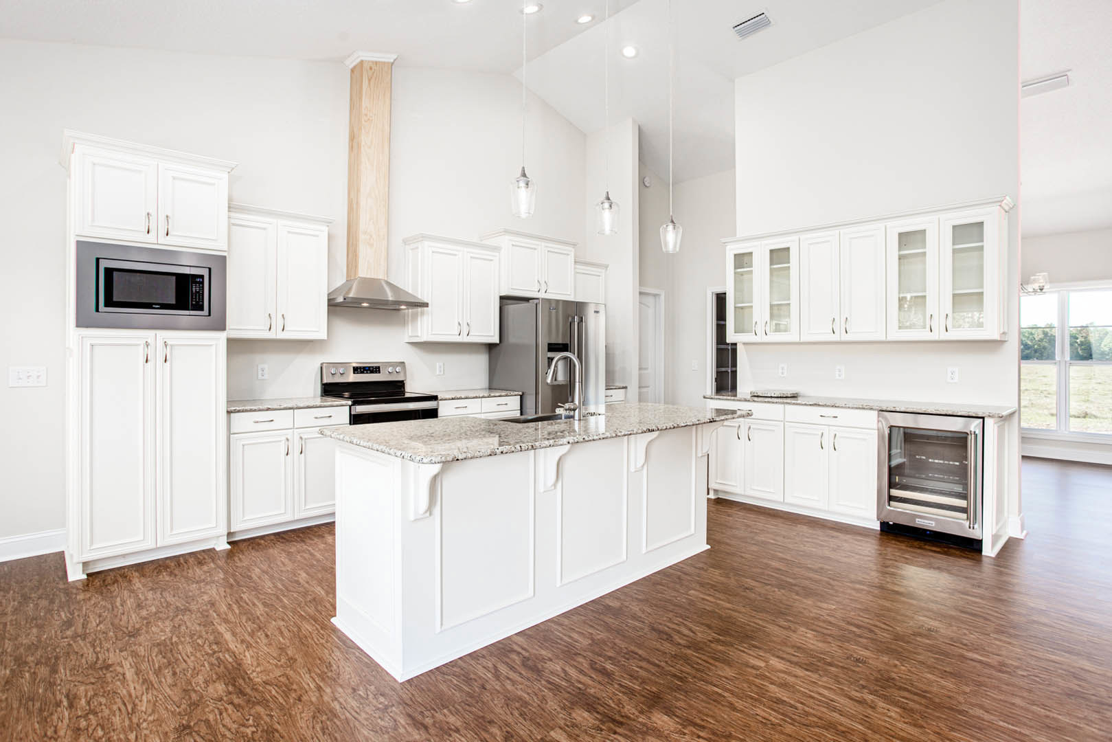 White kitchen cabinets, stainless steel refrigerator and microwave, granite-topped island, wood flooring, white oven, and upper cupboards