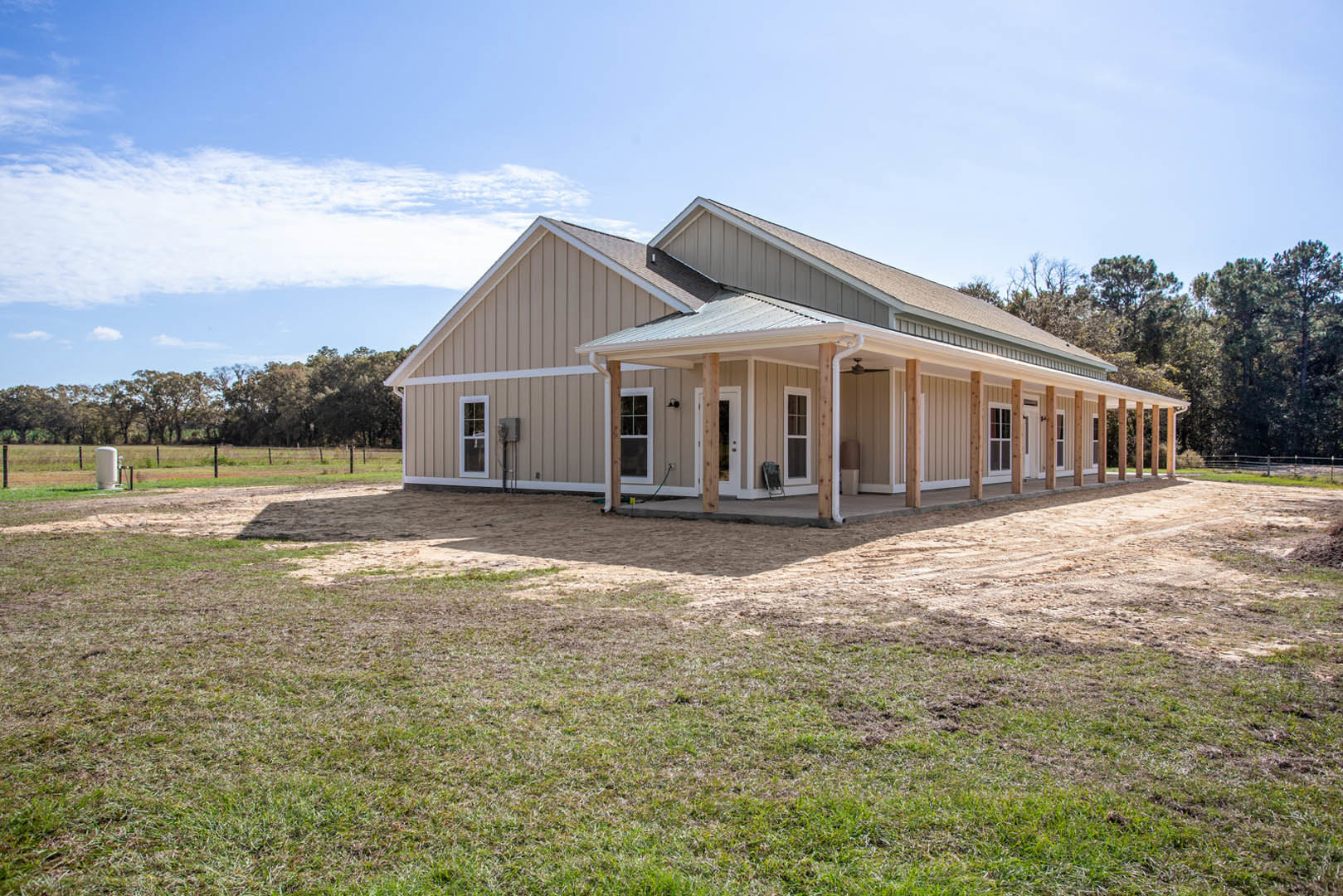 White-roofed house with covered porch, expansive grassy yard, mature trees, and partly cloudy sky