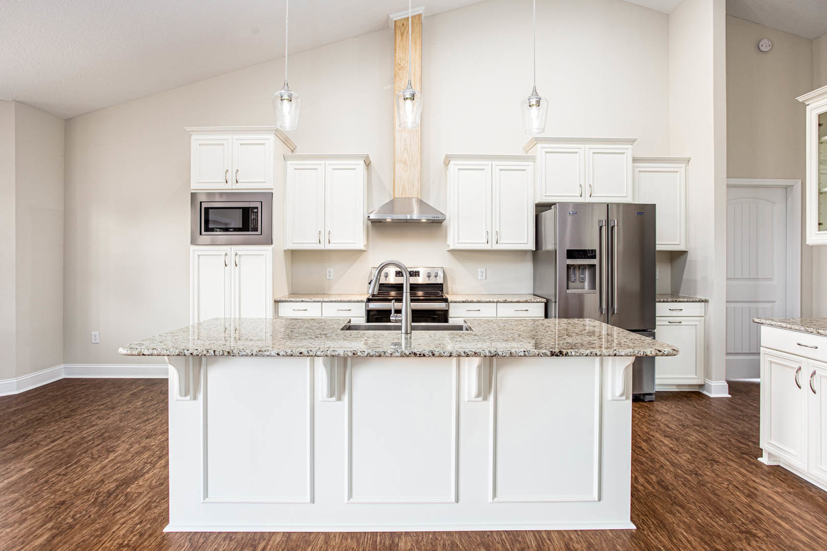Marble island with waterfall edge, white cabinetry, stainless steel refrigerator, built-in microwave, granite countertops, chrome faucet, light wood flooring