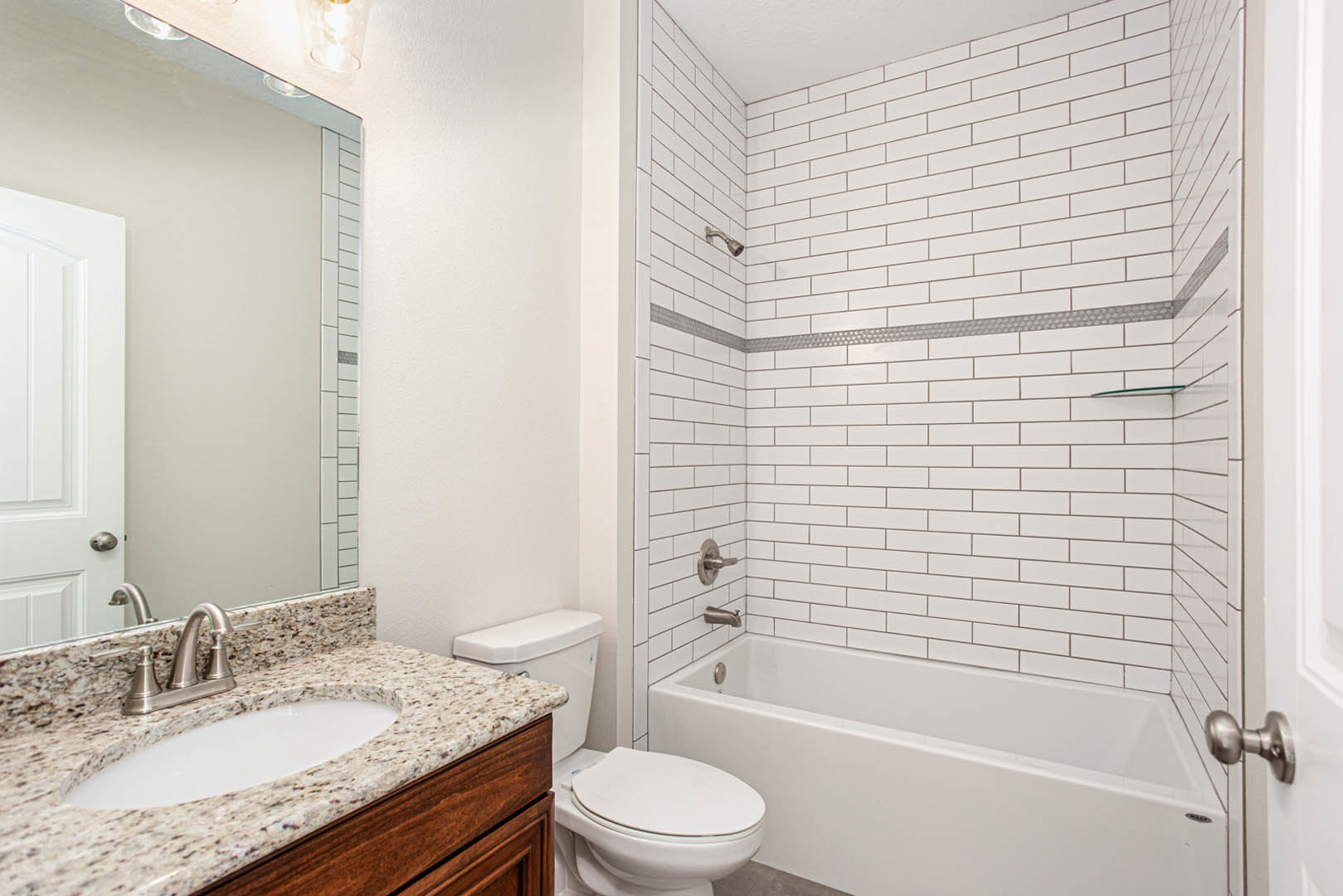 Modern bathroom with white porcelain sink, chrome faucet, wall-mounted mirror, white toilet beside a built-in bathtub, and light gray tile walls
