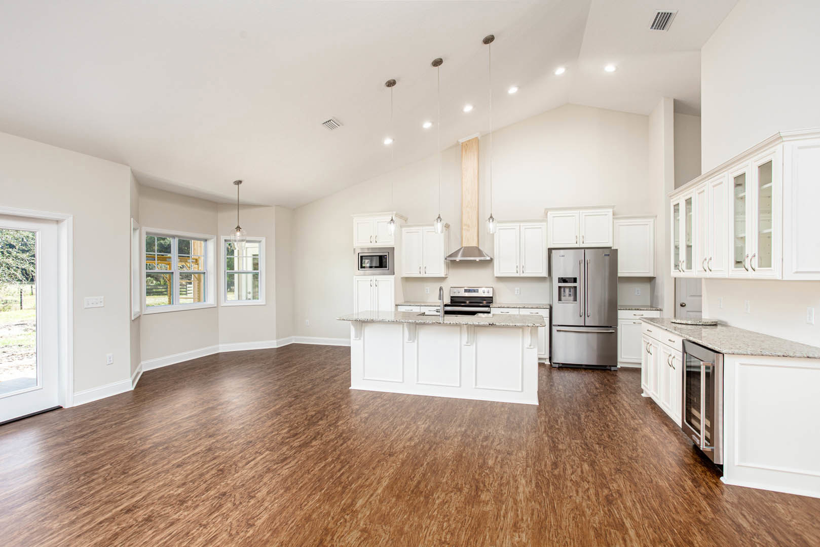 Spacious kitchen featuring wood flooring, white cabinetry, marble-topped island, stainless steel refrigerator and microwave, white walls, and ceiling vent