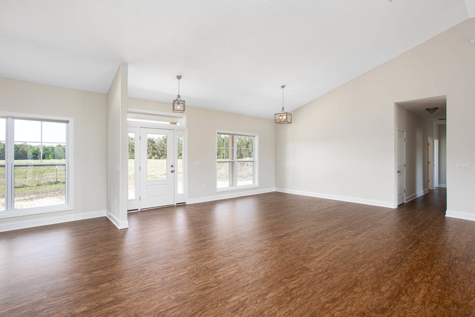 Spacious room featuring hardwood flooring, white walls, large window overlooking a field, and minimal furnishings