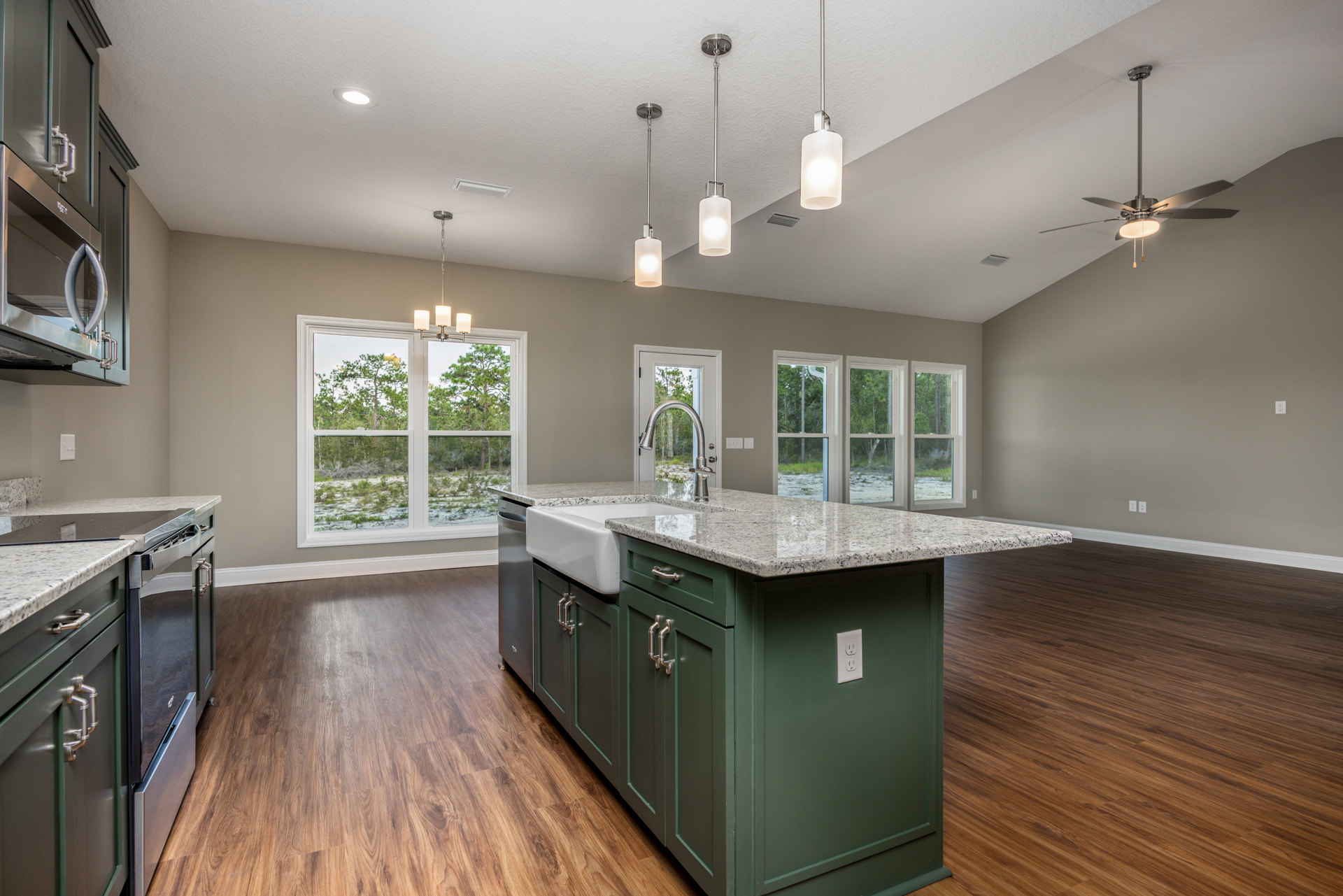 Spacious kitchen featuring a large central island with built-in sink, white countertops, wood cabinetry, stainless steel fixtures, wall-mounted light, and a window overlooking