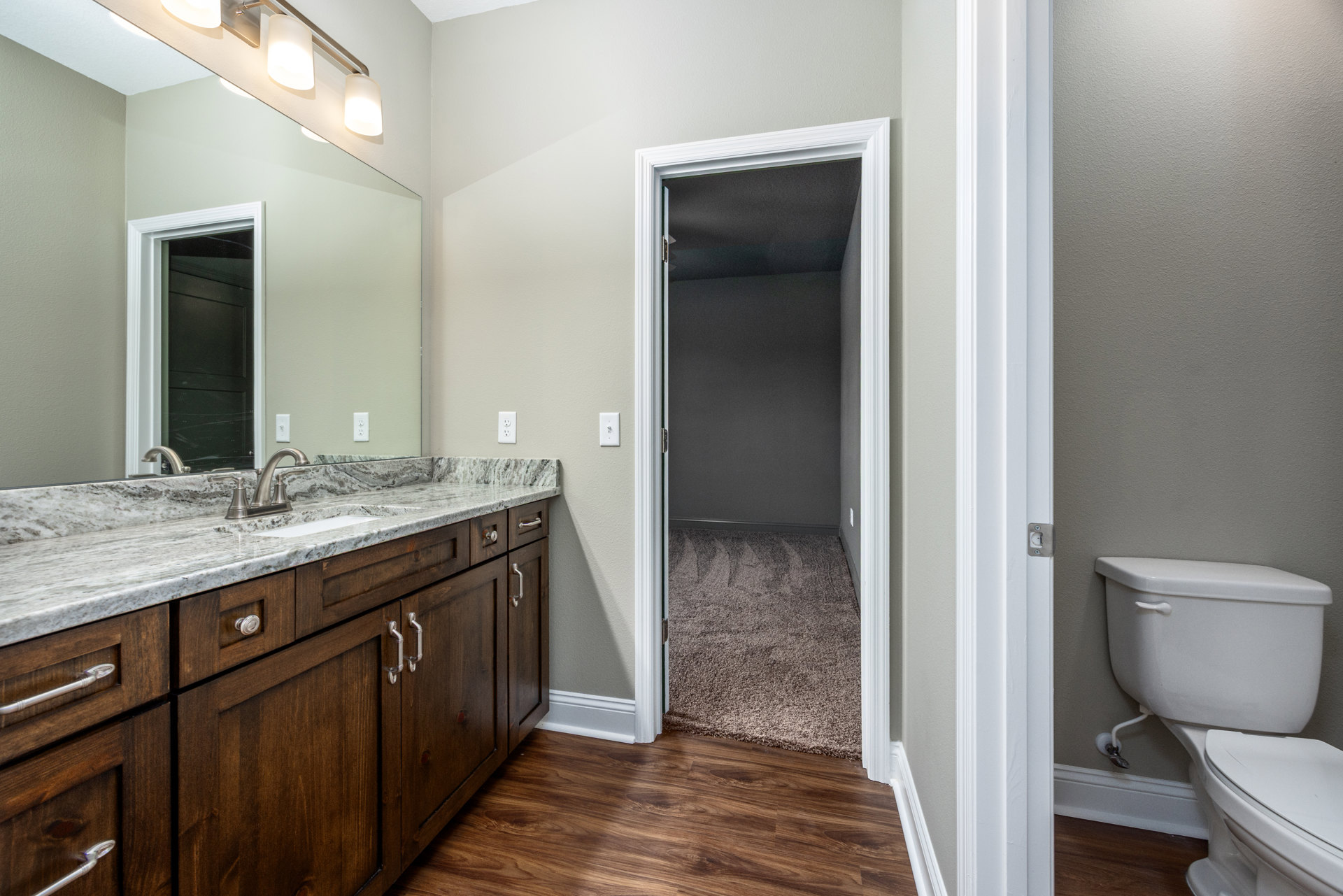 Bathroom with open door, white toilet and tank, marble countertop with cabinetry, tile flooring, wall-mounted tap and plumbing fixtures