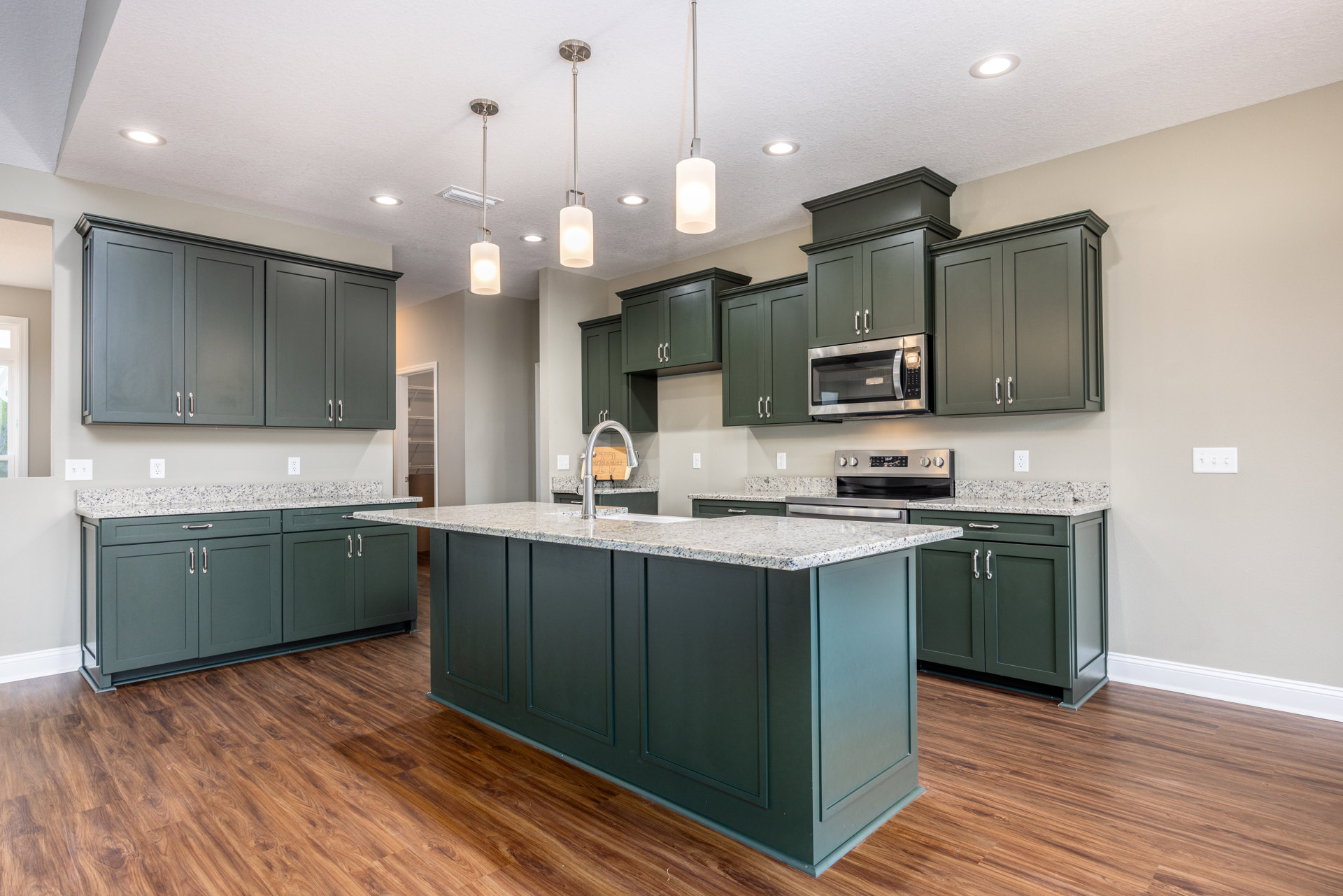 Spacious kitchen featuring a large central island with built-in sink, wood flooring, white cabinetry, stainless steel microwave, and modern rectangular wall lighting
