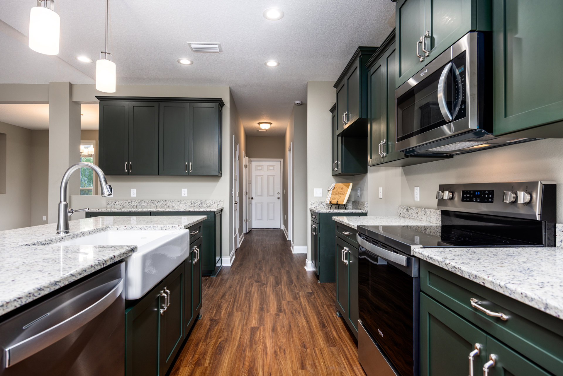 Kitchen with dark wood cabinets, granite countertops, stainless steel microwave, white door with silver knobs, black cabinetry with silver handles, chrome faucet, and wood cutting