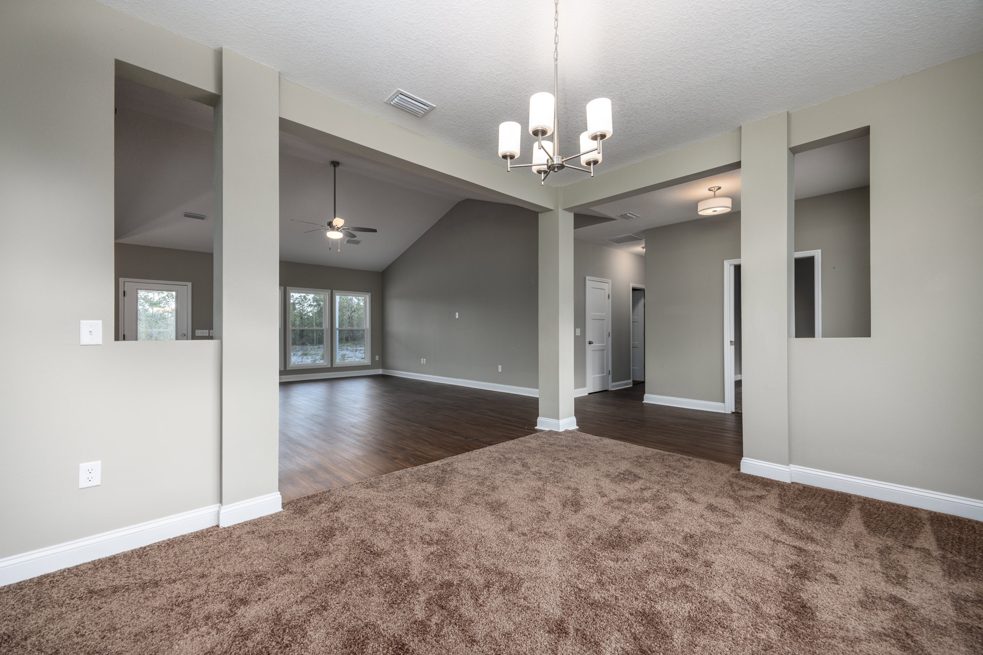 Carpeted room with a crystal chandelier, white paneled door with glass, large window overlooking trees, and decorative ceiling molding