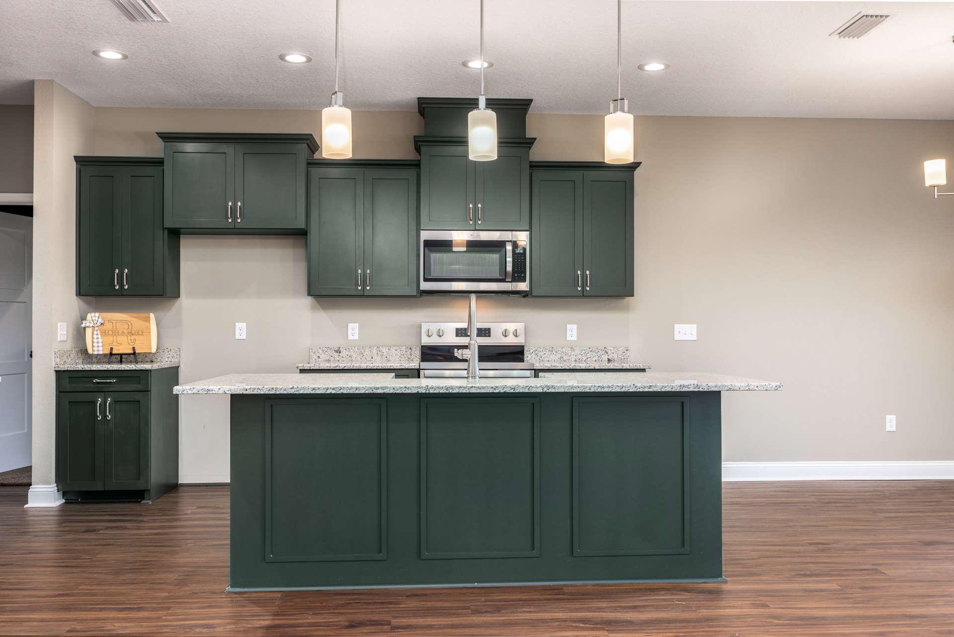 Marble countertop kitchen with wood flooring, white cabinetry, stainless steel microwave, chrome faucet on kitchen island, and modern light fixture