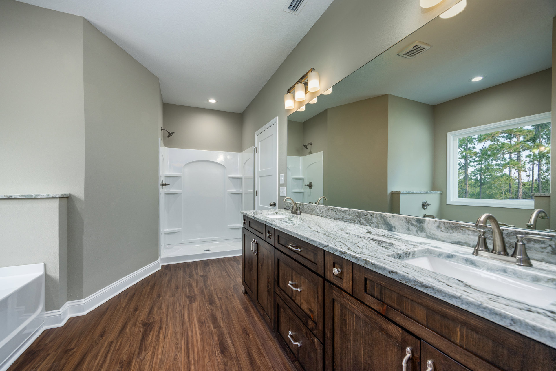 Bathroom with marble countertop and undermount sink, expansive wall mirror, white shower stall with glass door, freestanding white bathtub, wood flooring, white baseboards, window