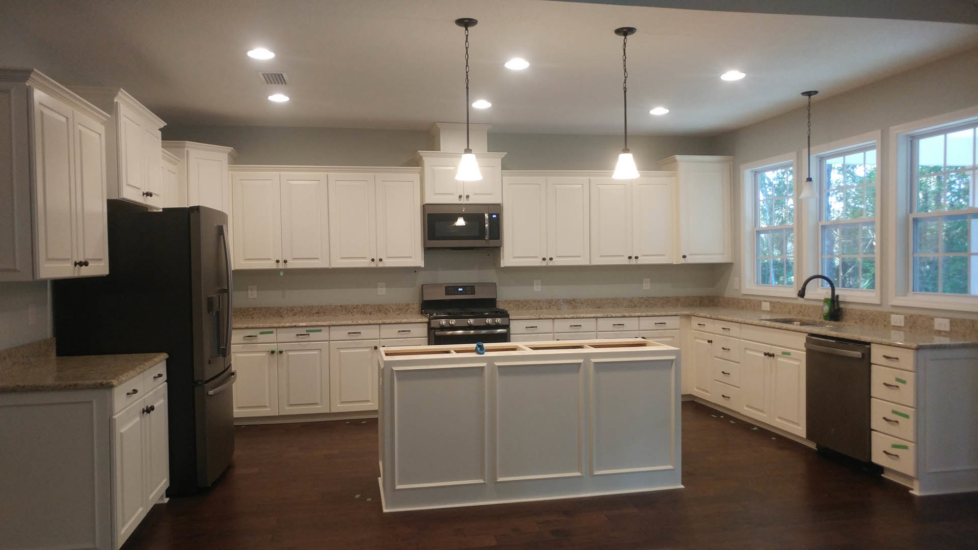 White kitchen cabinets, black refrigerator, stainless steel stove, built-in microwave with illuminated display, light fixture mounted on metal pole, blue tape on cabinet door