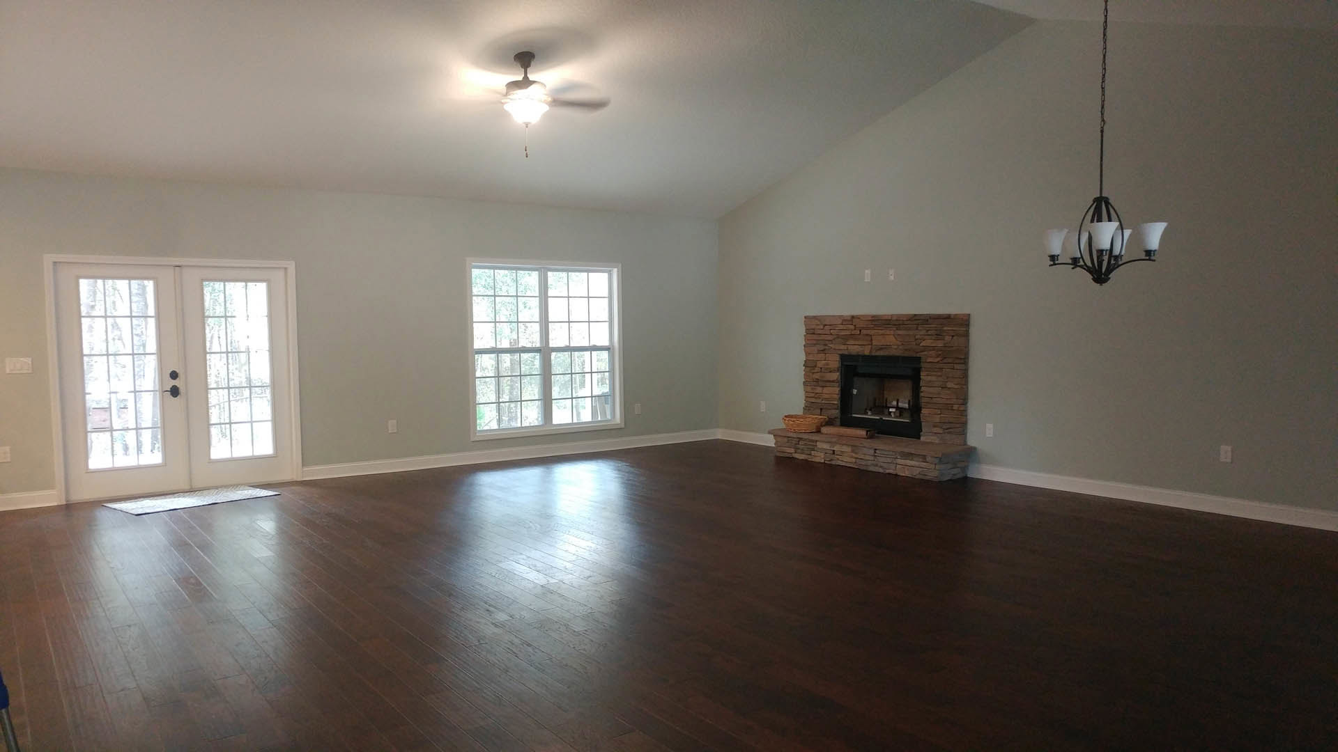 Hardwood floor living room featuring a black rectangular fireplace with glass window, ceiling fan, multi-pane window, and double glass-paned doors; basket placed beside fireplace.