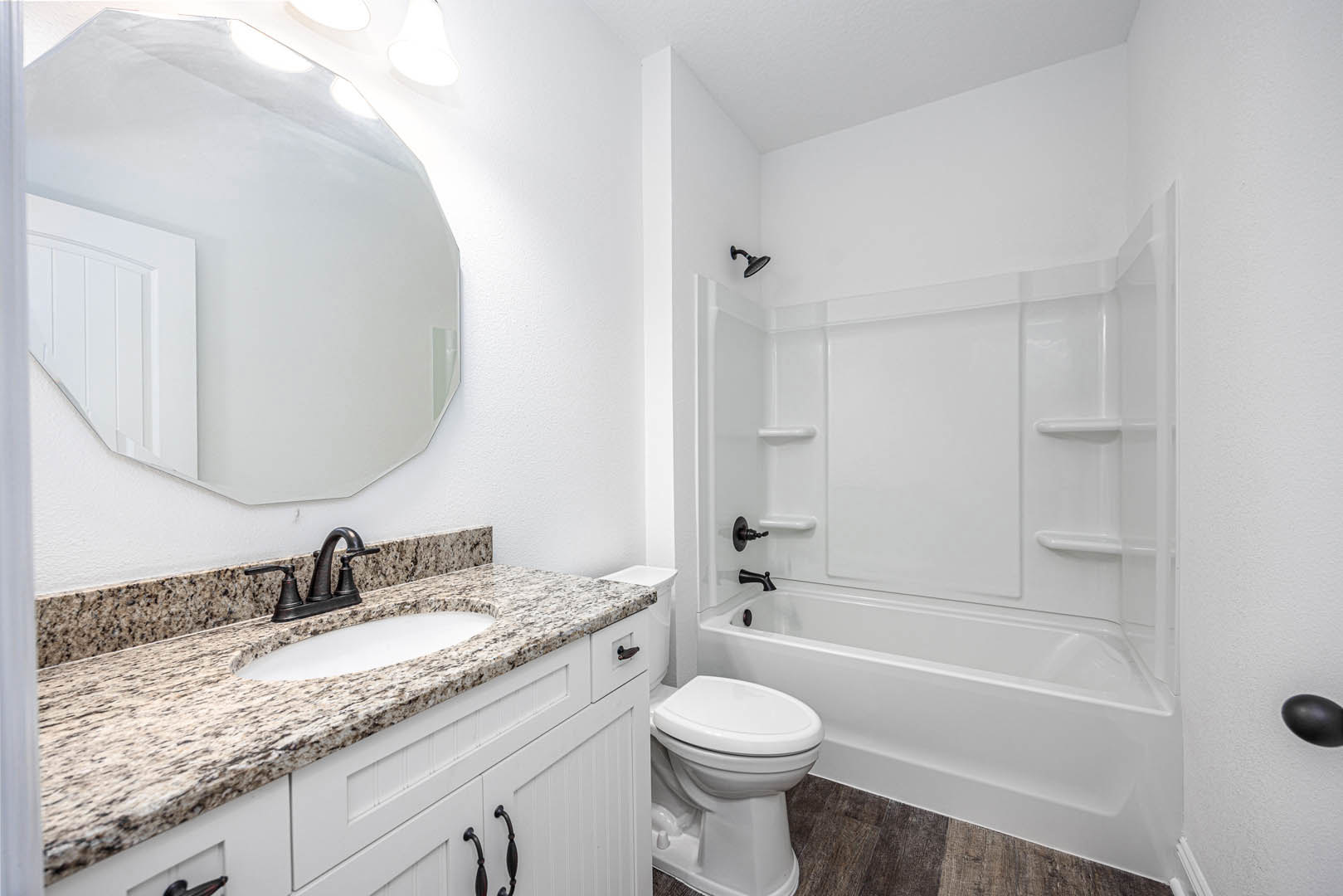 White porcelain sink set in a dark wood vanity with chrome faucet, rectangular wall mirror above, white toilet with closed lid, light gray tile flooring, and neutral painted walls
