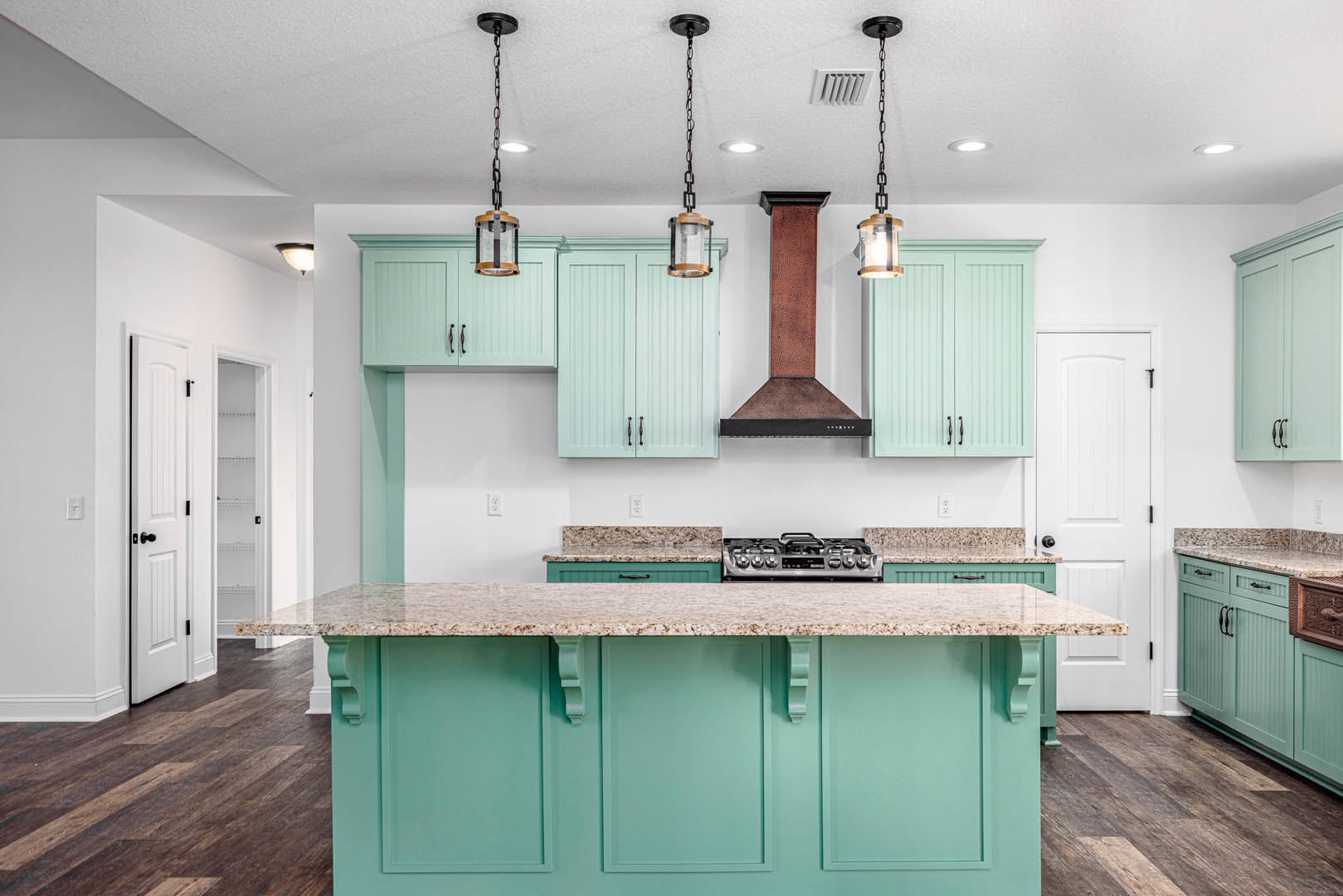Modern kitchen featuring a marble island with built-in stove, white cabinetry, stainless steel sink, and pendant light fixture suspended by a black chain.