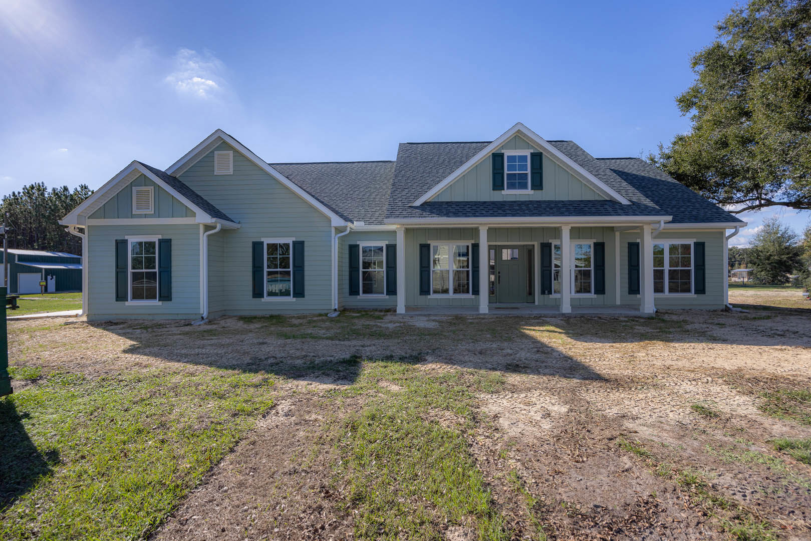 Two-story home with gray siding, white trim, gabled roof, large windows, covered front porch, and manicured lawn with trees in the background