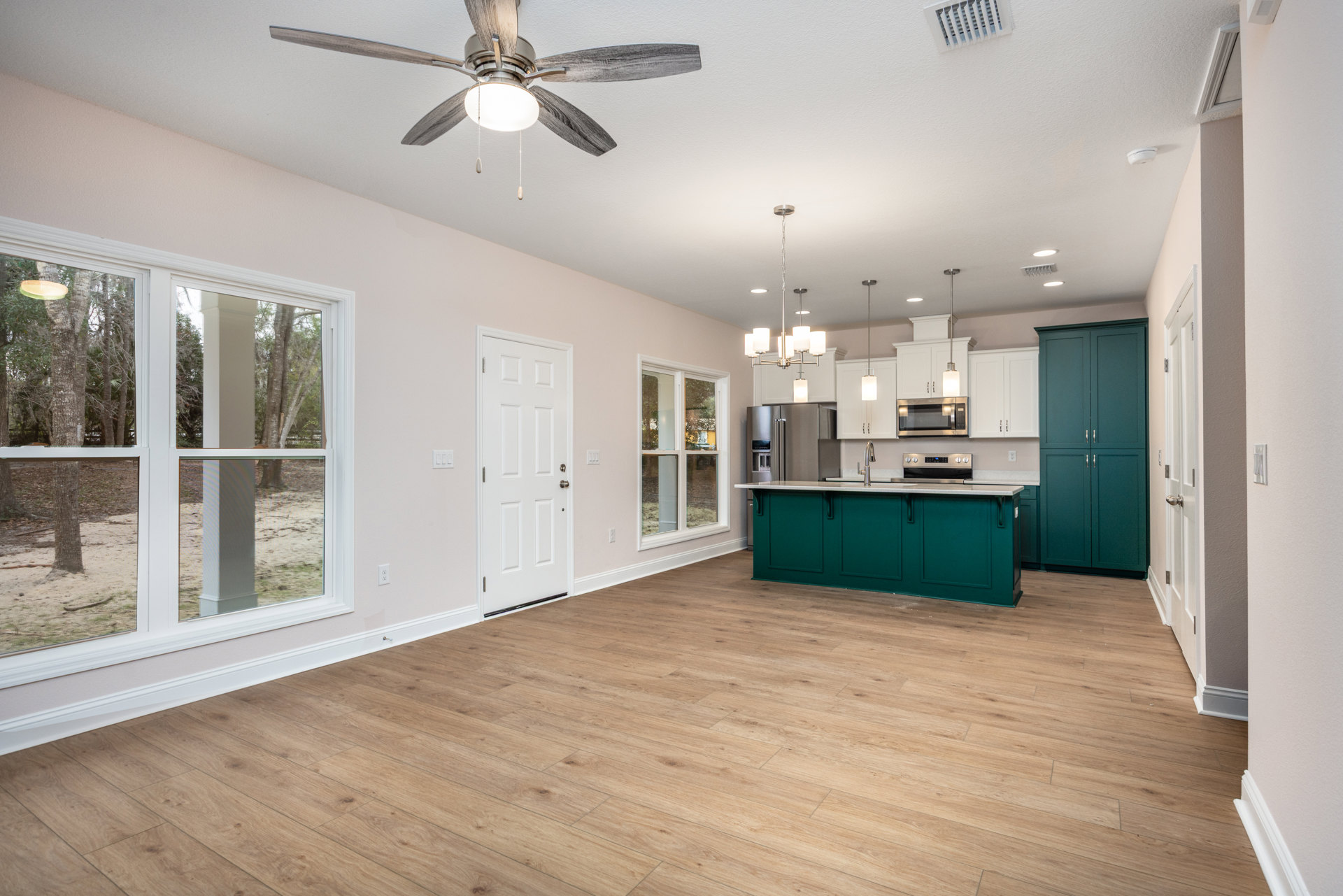Open kitchen and living room featuring a ceiling fan with light fixture, green cabinetry with silver handles, wood flooring, green and white doors with silver handles, and a