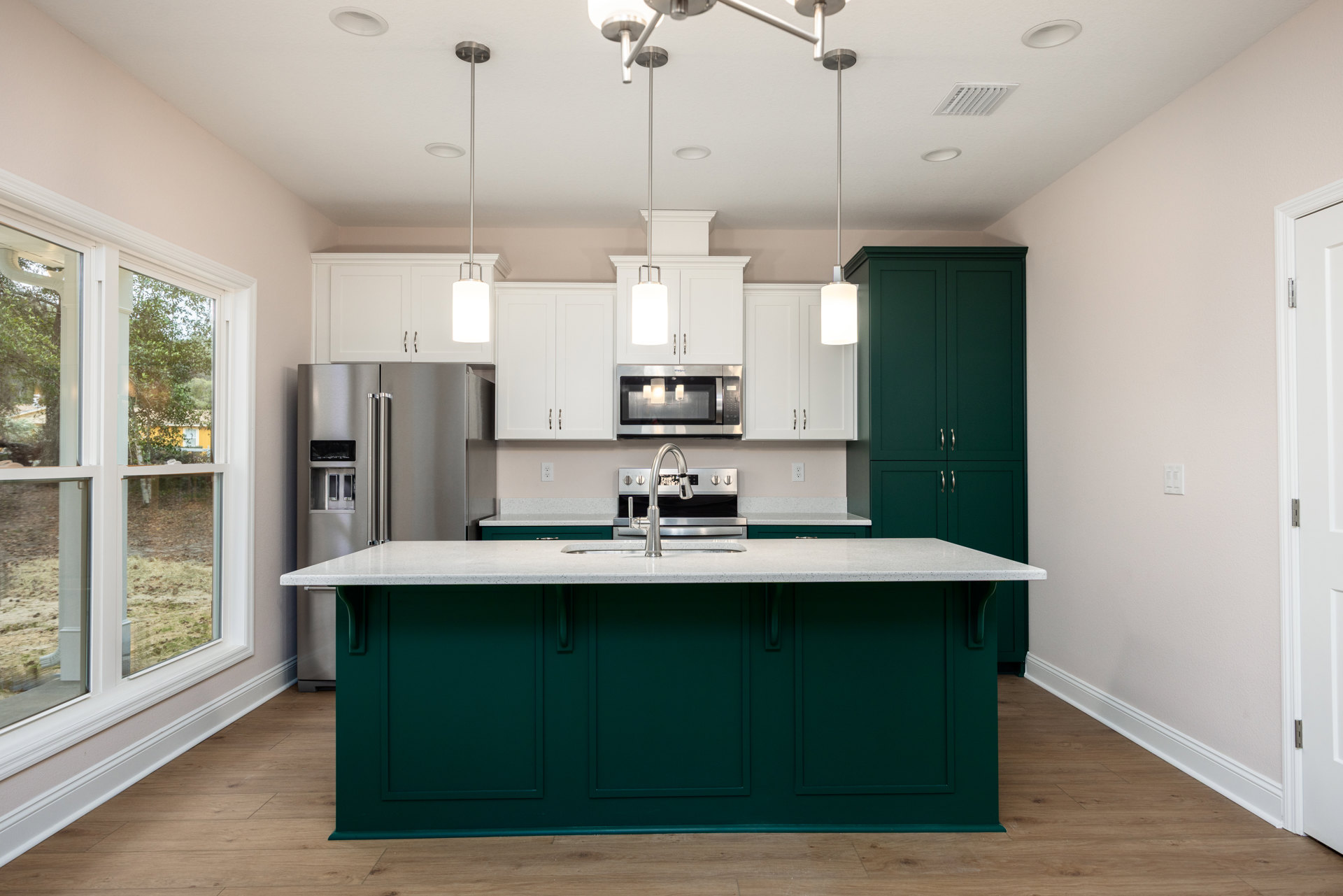 Green kitchen island with white quartz countertop, stainless steel faucet, built-in microwave, white cabinetry, stove, and large window overlooking grassy field
