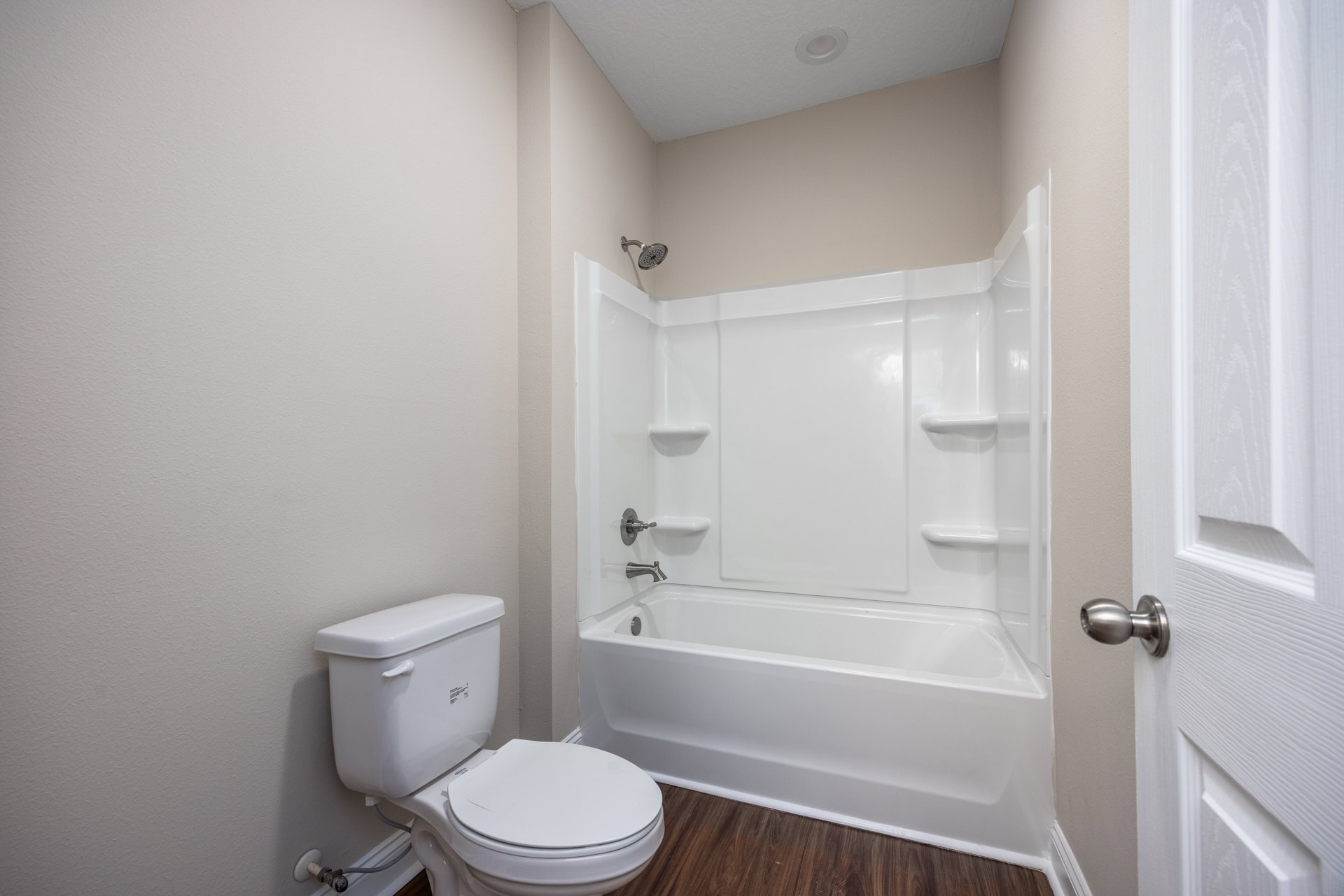 White toilet with lid up beside a rectangular white bathtub, light-colored tile flooring, white door with silver knob, neutral painted walls