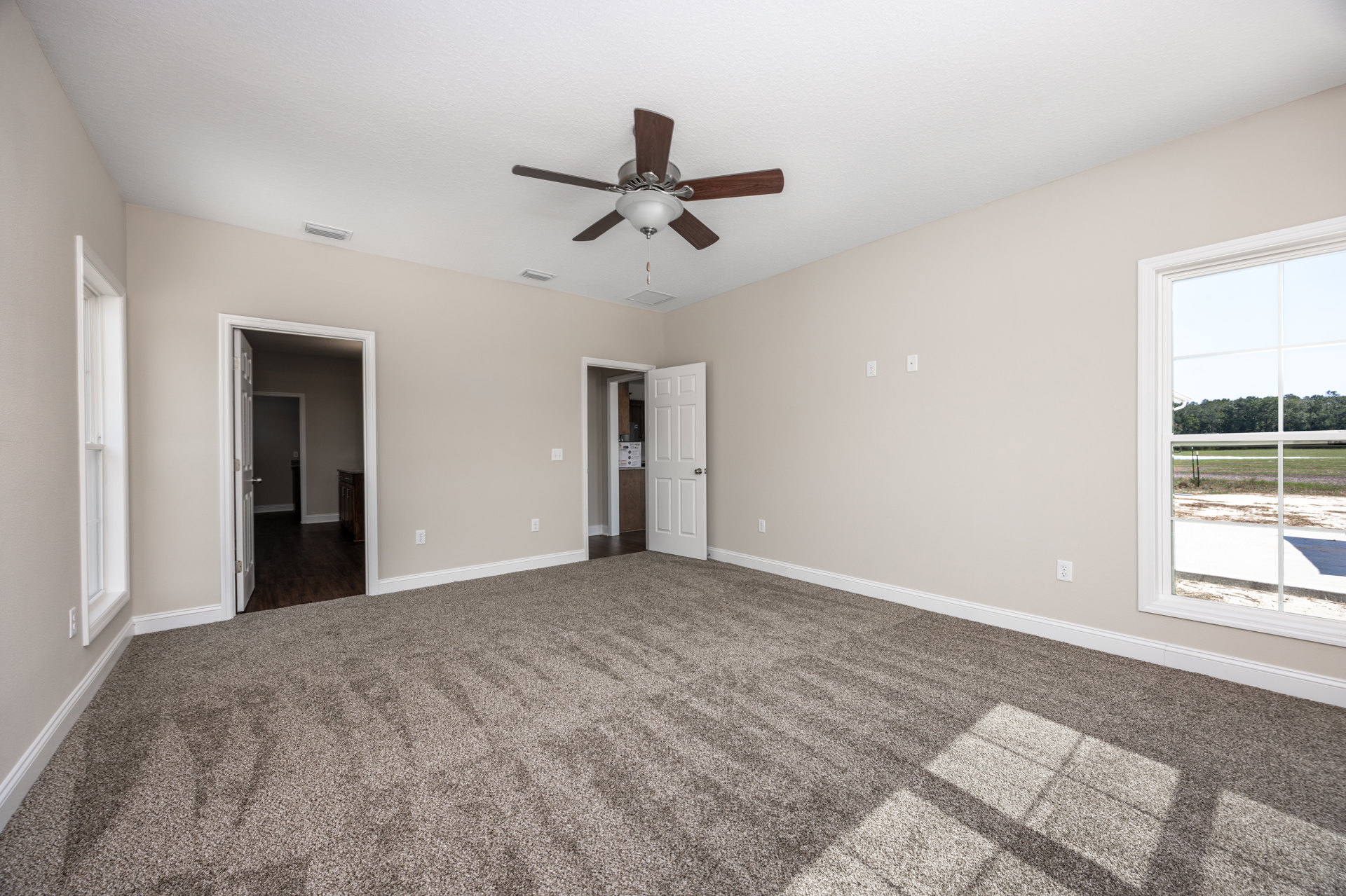 Carpeted bedroom with a ceiling fan and light fixture, white walls, and an open white door with a silver knob leading to an adjacent room