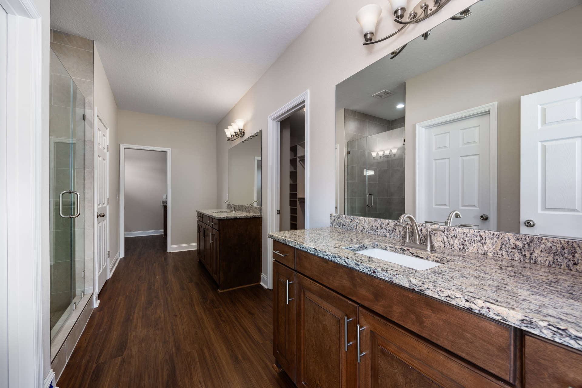 Bathroom with marble countertop, wood flooring, white sink, large mirror, and white paneled door