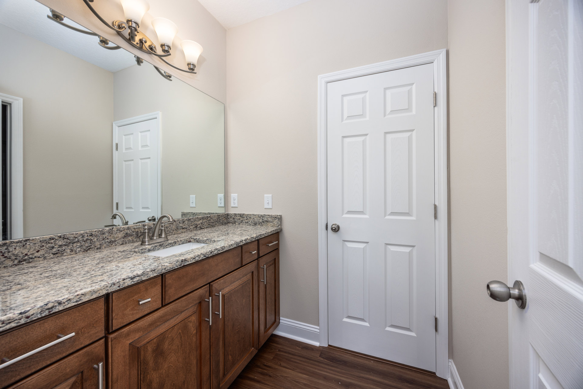 Bathroom featuring a white paneled door with silver knob, marble countertop with undermount sink, white cabinetry, and light-colored tile backsplash