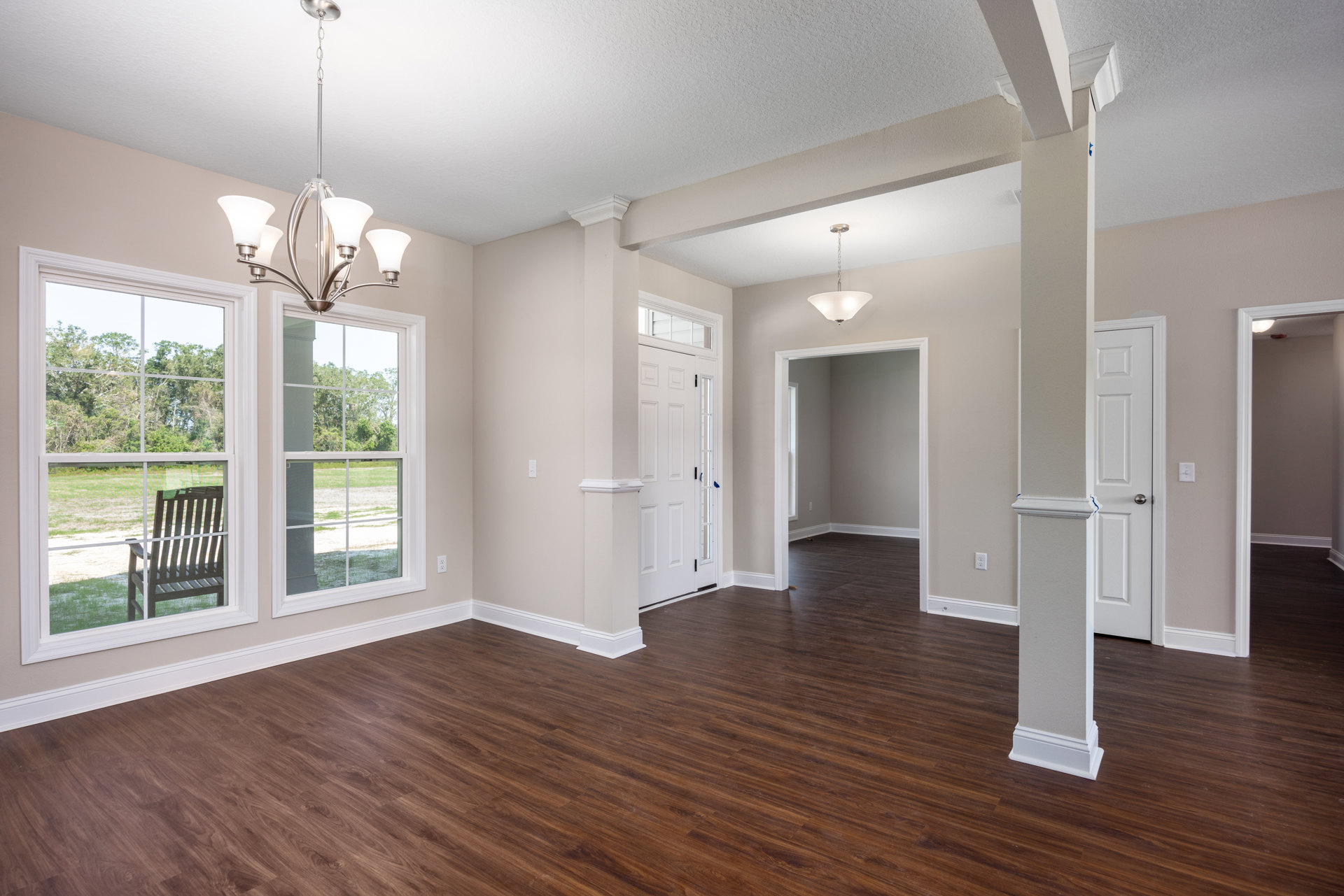Wood floor with white walls, white pillar, hanging chandelier, and window with wooden chair outside