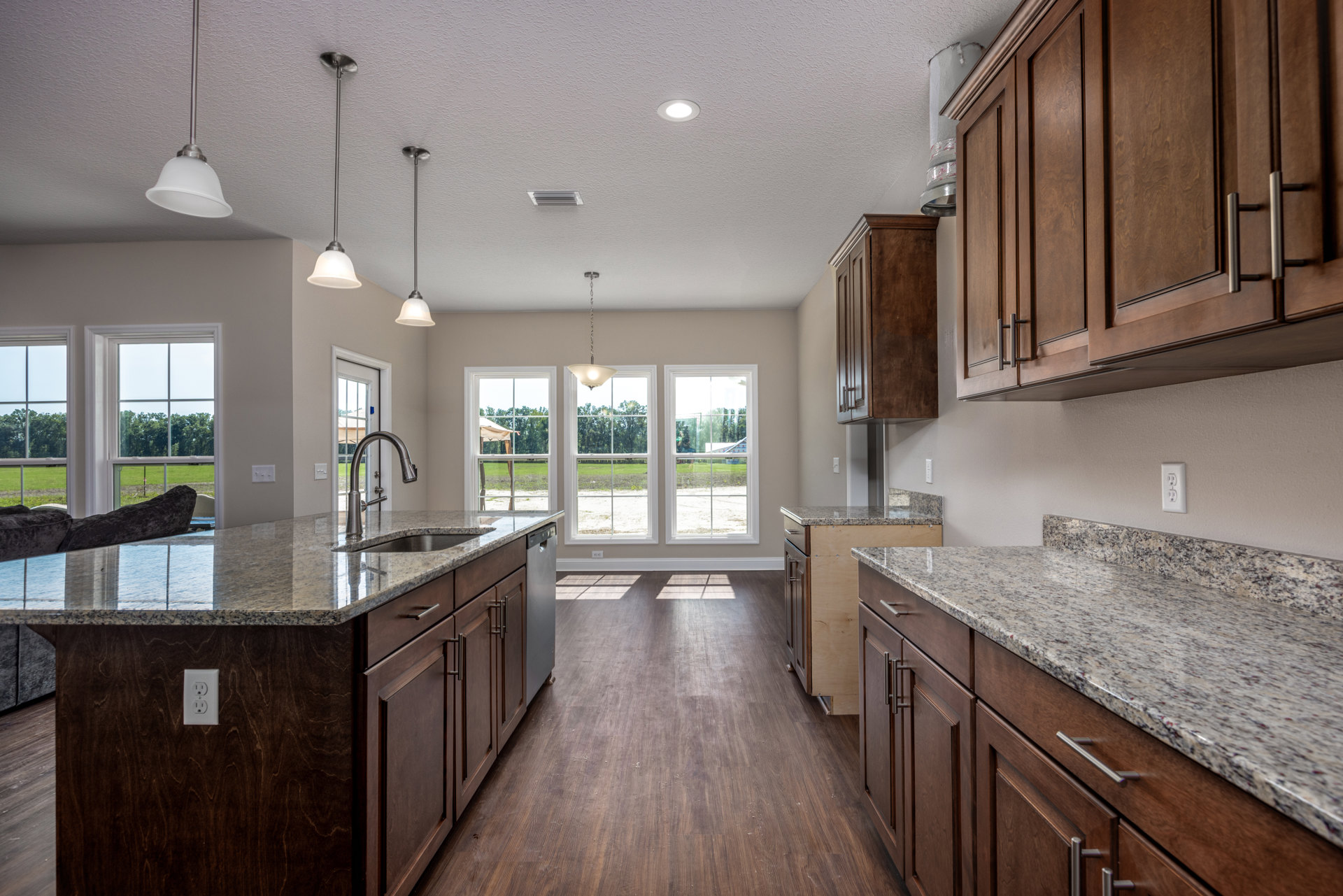Granite countertops with marbled surface, white cabinetry, stainless steel sink, modern light fixture, electrical outlet, and metal bar mounted on wall