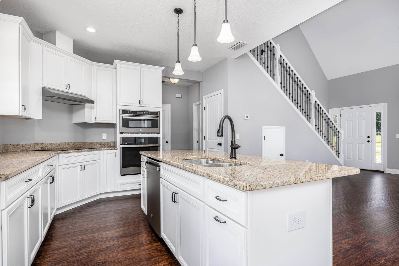 White kitchen cabinets with marble countertops, stainless steel microwave and oven, wooden flooring, pendant ceiling lights, chrome faucet, and built-in cabinetry