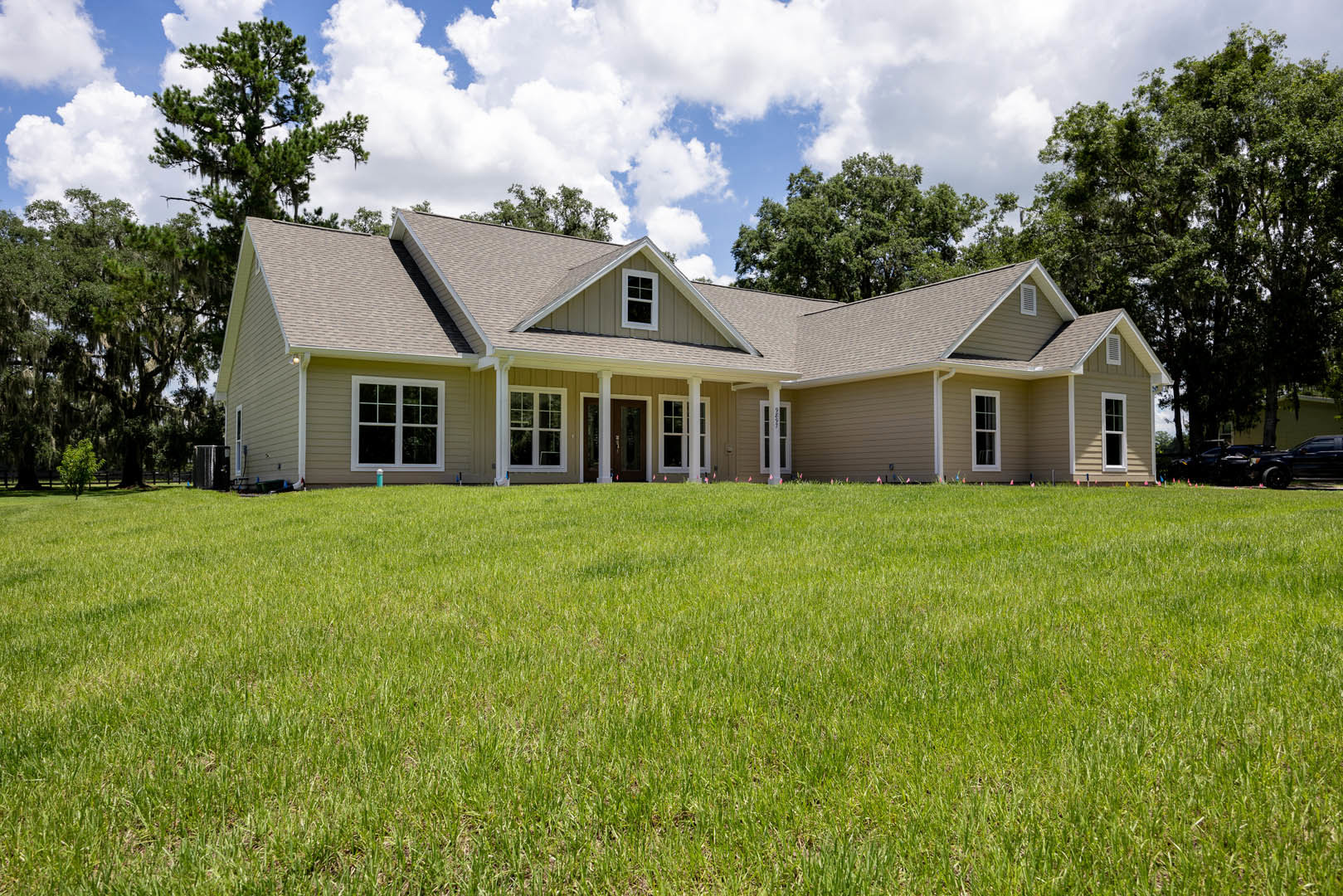 Two-story white house with gabled roof, covered front porch, and manicured green lawn bordered by mature trees under a partly cloudy sky.