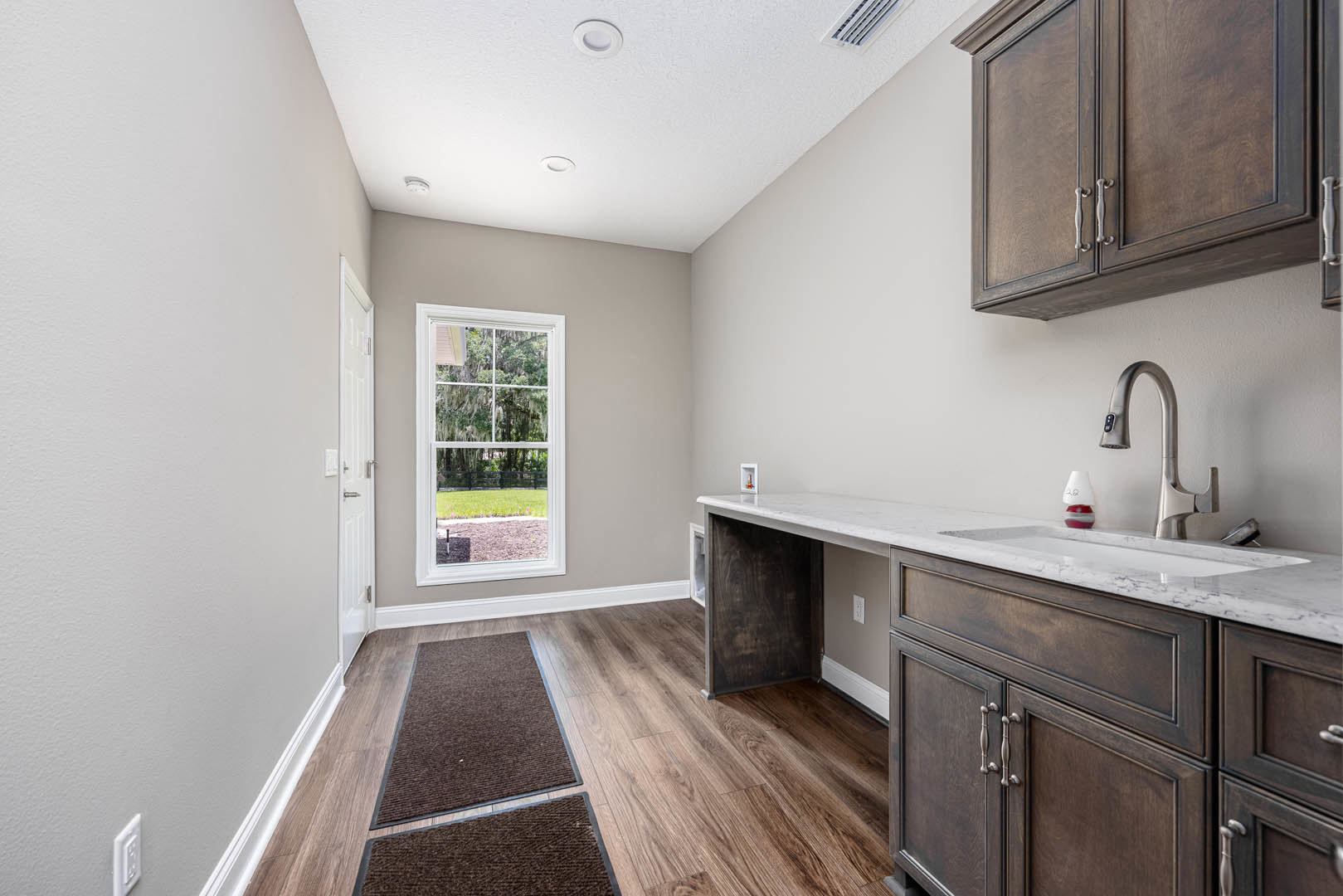 Kitchen with granite countertop, stainless steel sink, wooden cabinetry, wood flooring, and window overlooking lawn and trees