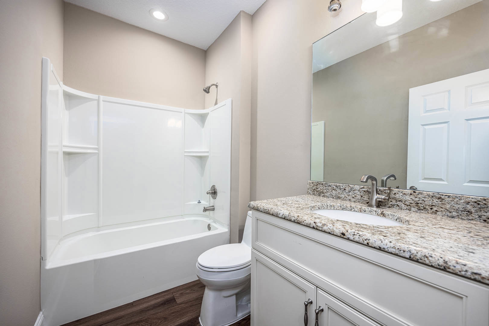 White tile bathroom featuring a built-in bathtub, modern sink with chrome faucet, white toilet, light-colored cabinetry, and stone countertop