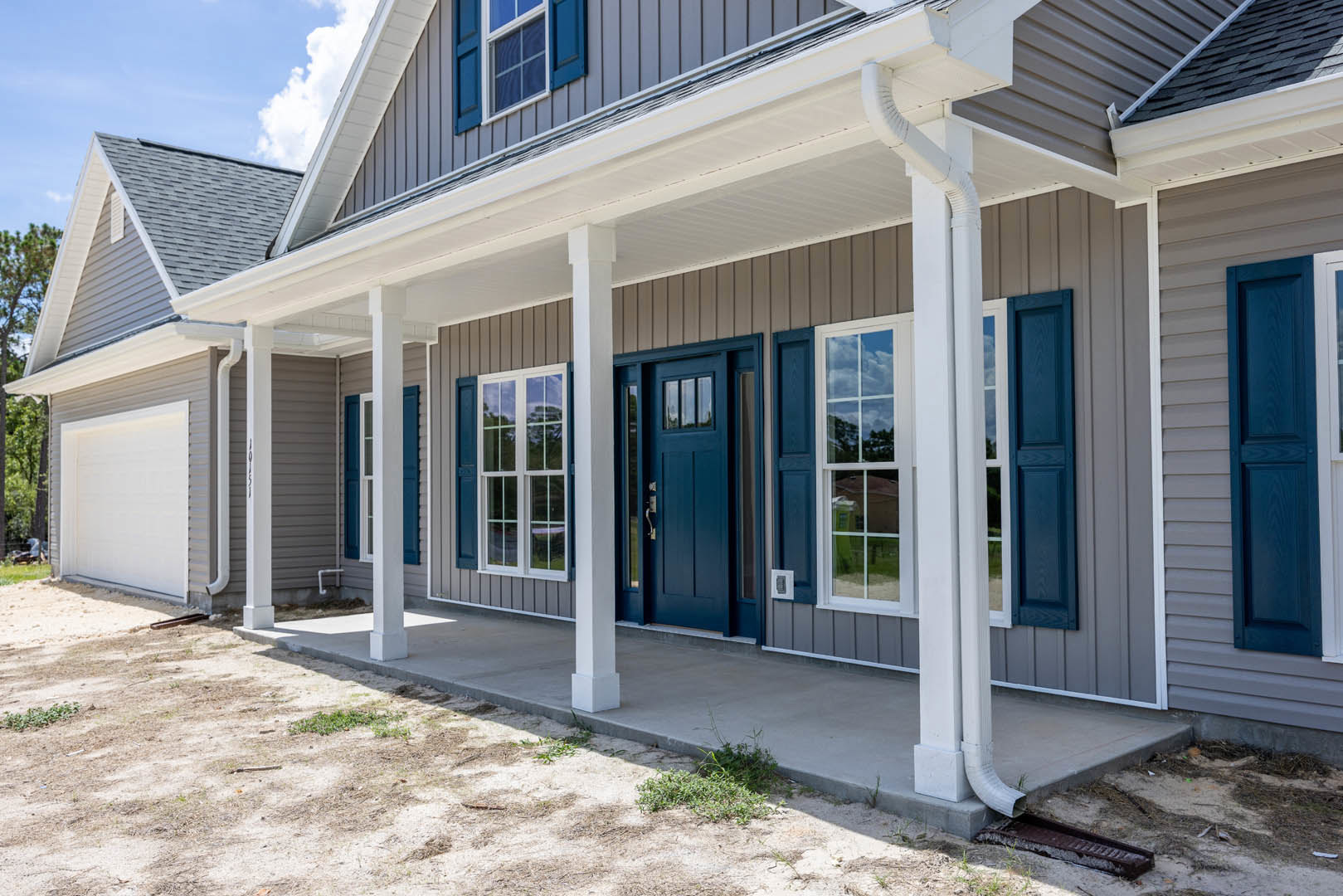 Blue front door framed by white pillars and porch, white siding exterior, sash window, and white awning above entry.