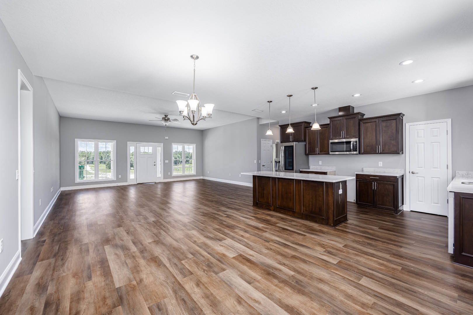Spacious open floor plan featuring hardwood flooring, central kitchen island with marble countertop, white cabinetry, stainless steel appliances, white door with silver handle