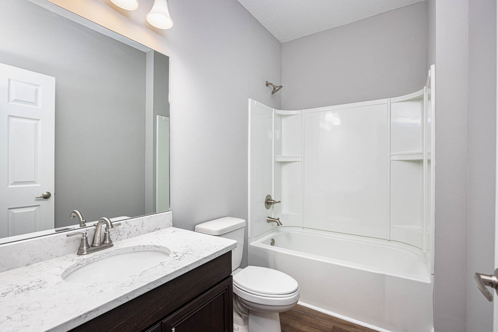 Bathroom with white freestanding tub, white sink with chrome faucet, white toilet, light tile flooring, wall-mounted mirror, and neutral wall finishes