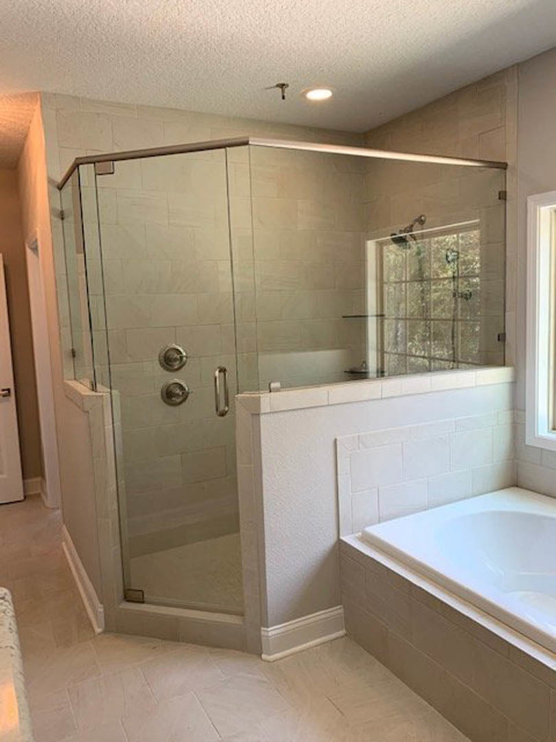 Bathroom featuring a frameless glass shower enclosure, freestanding white bathtub, light tile flooring, and modern chrome fixtures