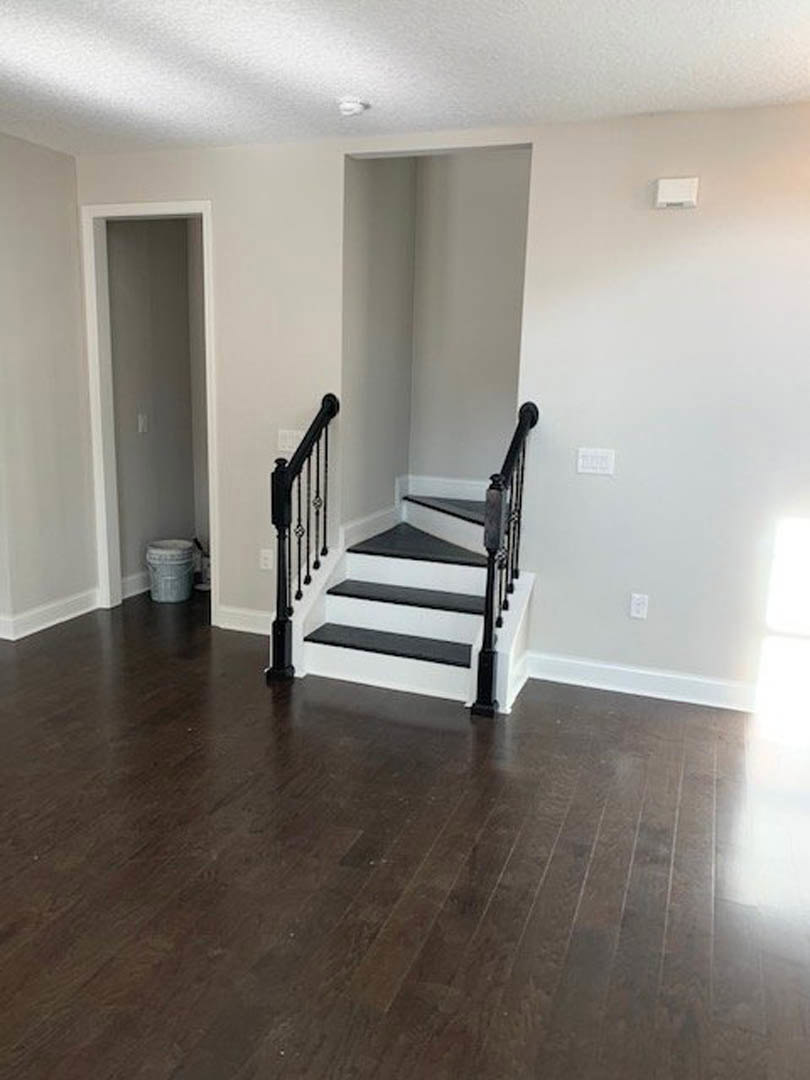 Black and white staircase with dark wood flooring, white walls, close-up of metal railing, white plastic storage container, and hallway light switch