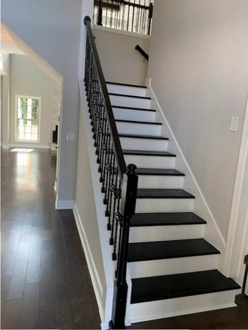 Black and white staircase with wood flooring, white trim, white-framed window, and close-up view of black handrail and balusters