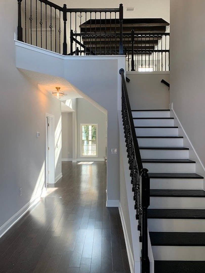 Dark wood staircase with black and white striped accent wall, white-framed window, and metal railing in hallway with matching dark wood flooring
