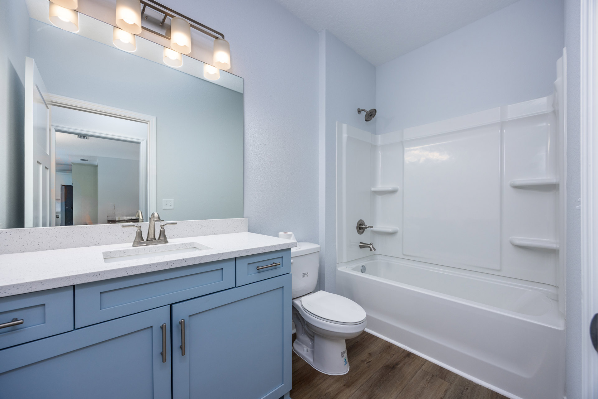 White tile bathroom with a freestanding bathtub, modern toilet with lid up, stone countertop and chrome faucet, overhead light fixture with white shade