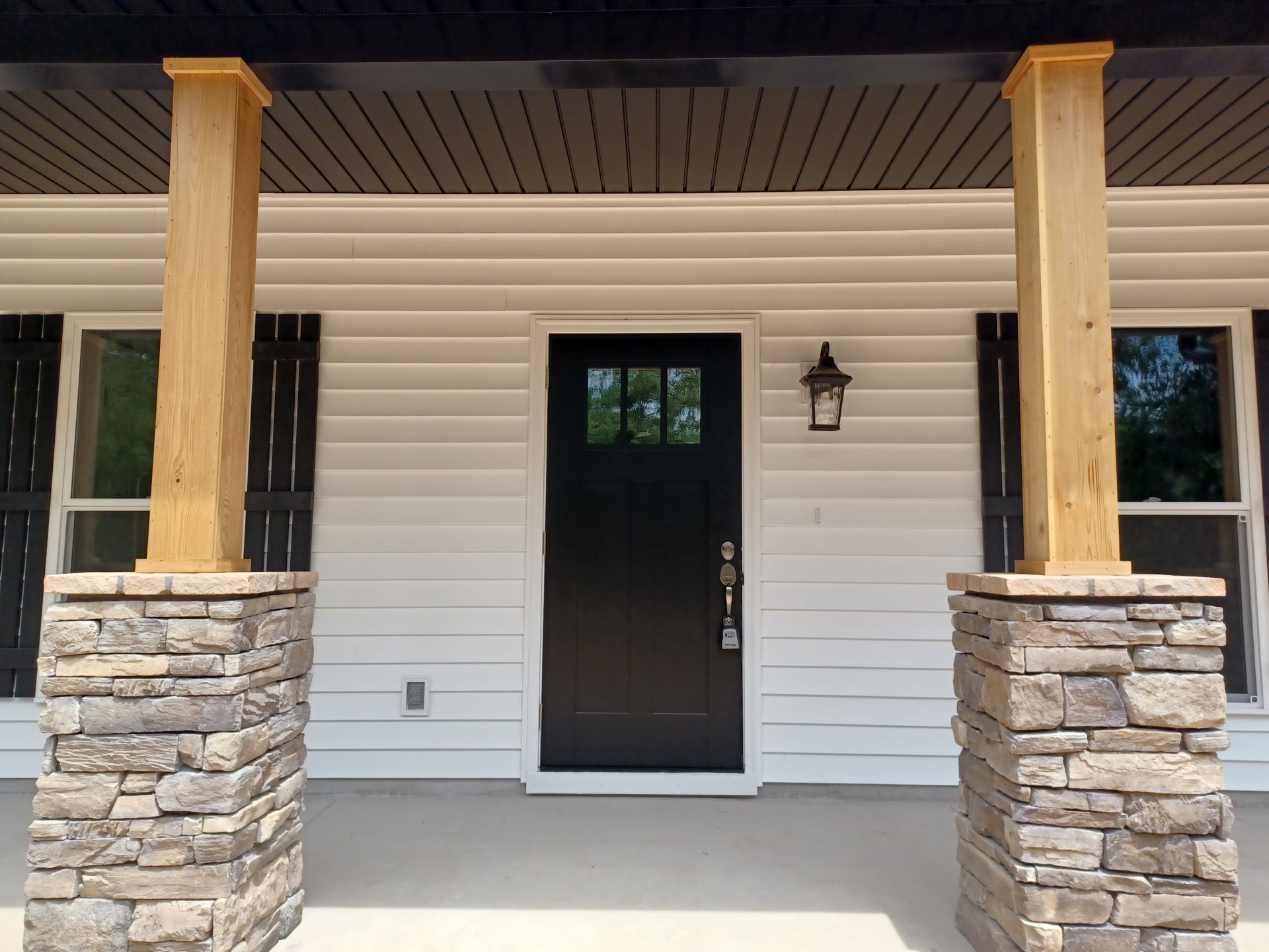 Black front door with keyhole, flanked by stone pillars topped with black caps, black lantern mounted beside door, white exterior walls, porch area visible.