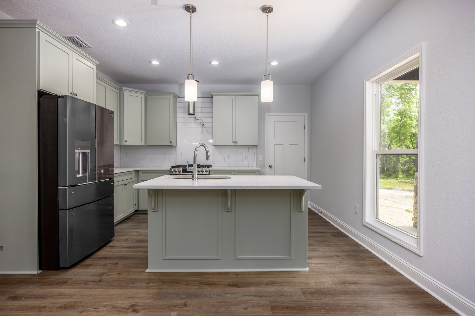 Spacious kitchen featuring a large central island with built-in sink and faucet, white cabinetry with silver hardware, stainless steel refrigerator, tile backsplash, and