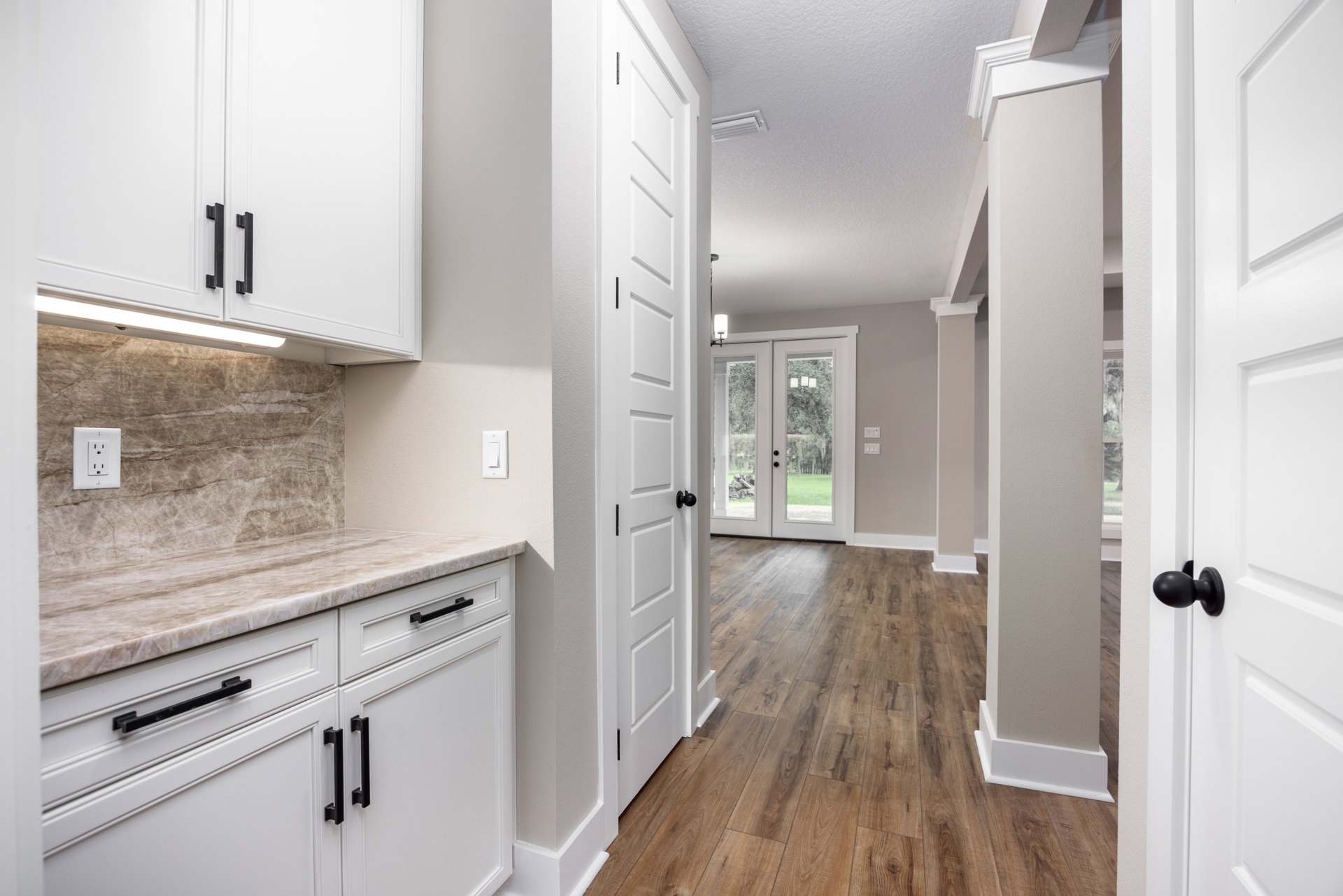 White kitchen with wood floors, white cabinets, white outlet, glass-paneled door opening to lawn, black door knob on white door, close-up of white cabinet and black handle