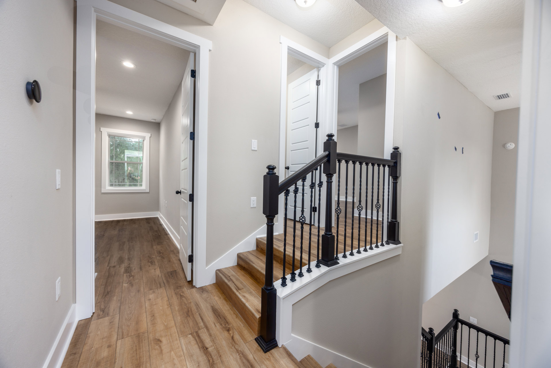 Staircase with black metal railings, laminate wood flooring, white plaster walls, and a white door with black hinges in a modern residential interior.