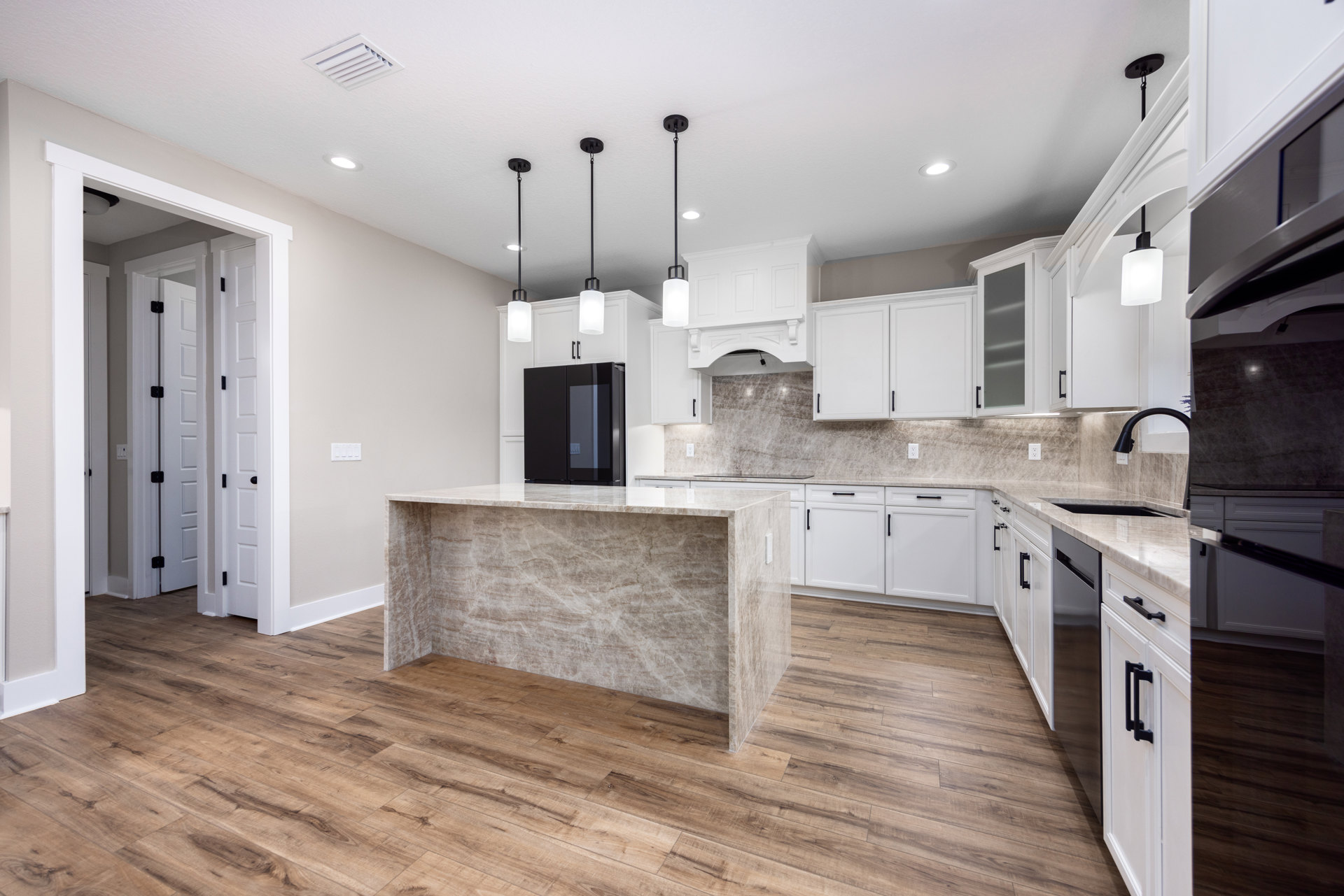 Marble kitchen island with waterfall edge, black refrigerator, glass-front black cabinet, wood flooring, modern light fixture, white walls, stainless steel sink