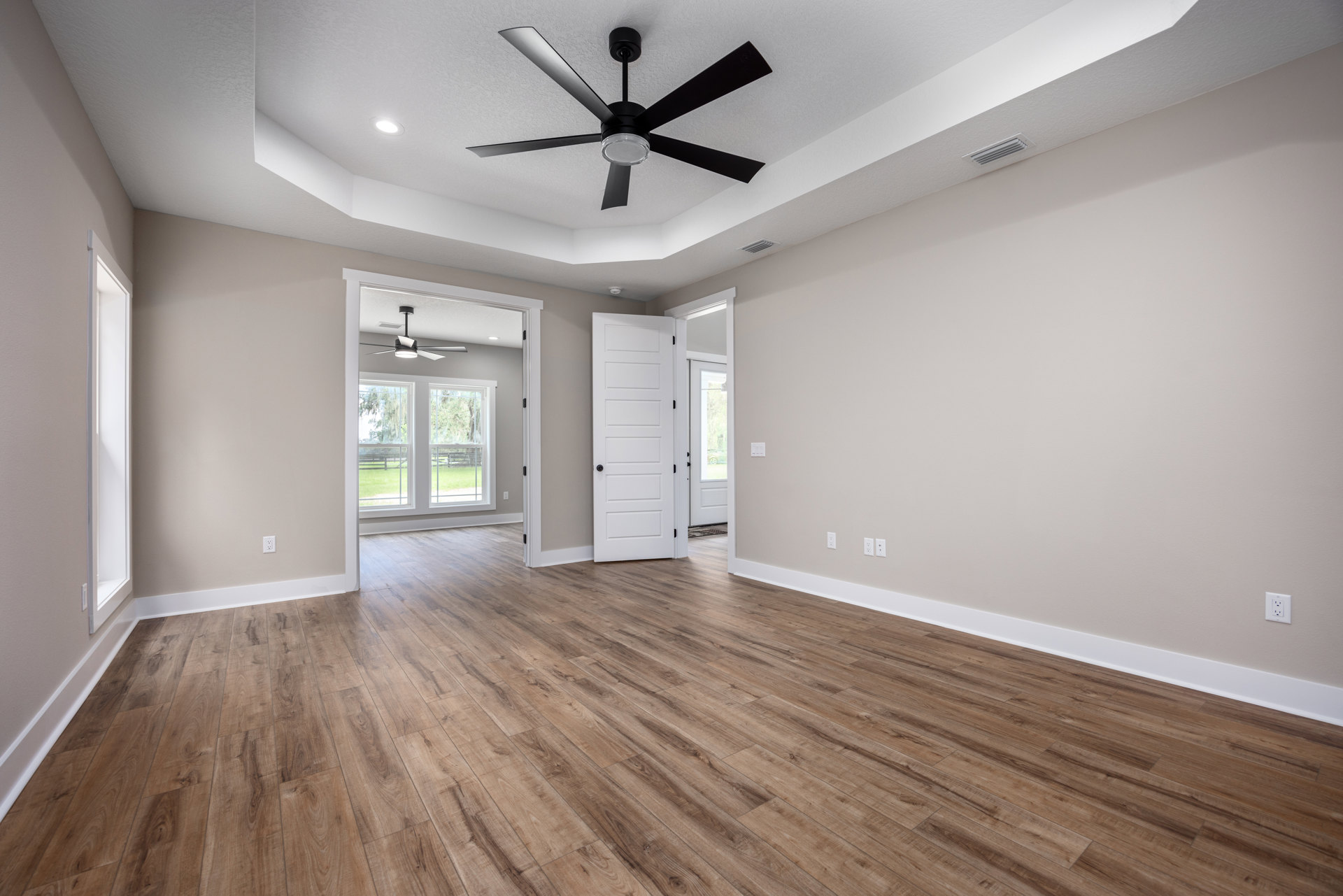 Ceiling fan with light fixture, wood flooring, white doors with black knobs, neutral walls, windows allowing natural light