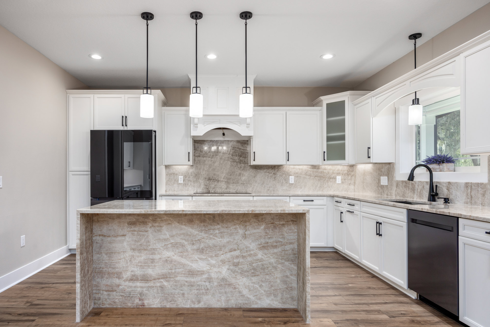 Marble countertops and white cabinetry in a modern kitchen with black refrigerator, tile backsplash, stainless steel sink, and light wood flooring